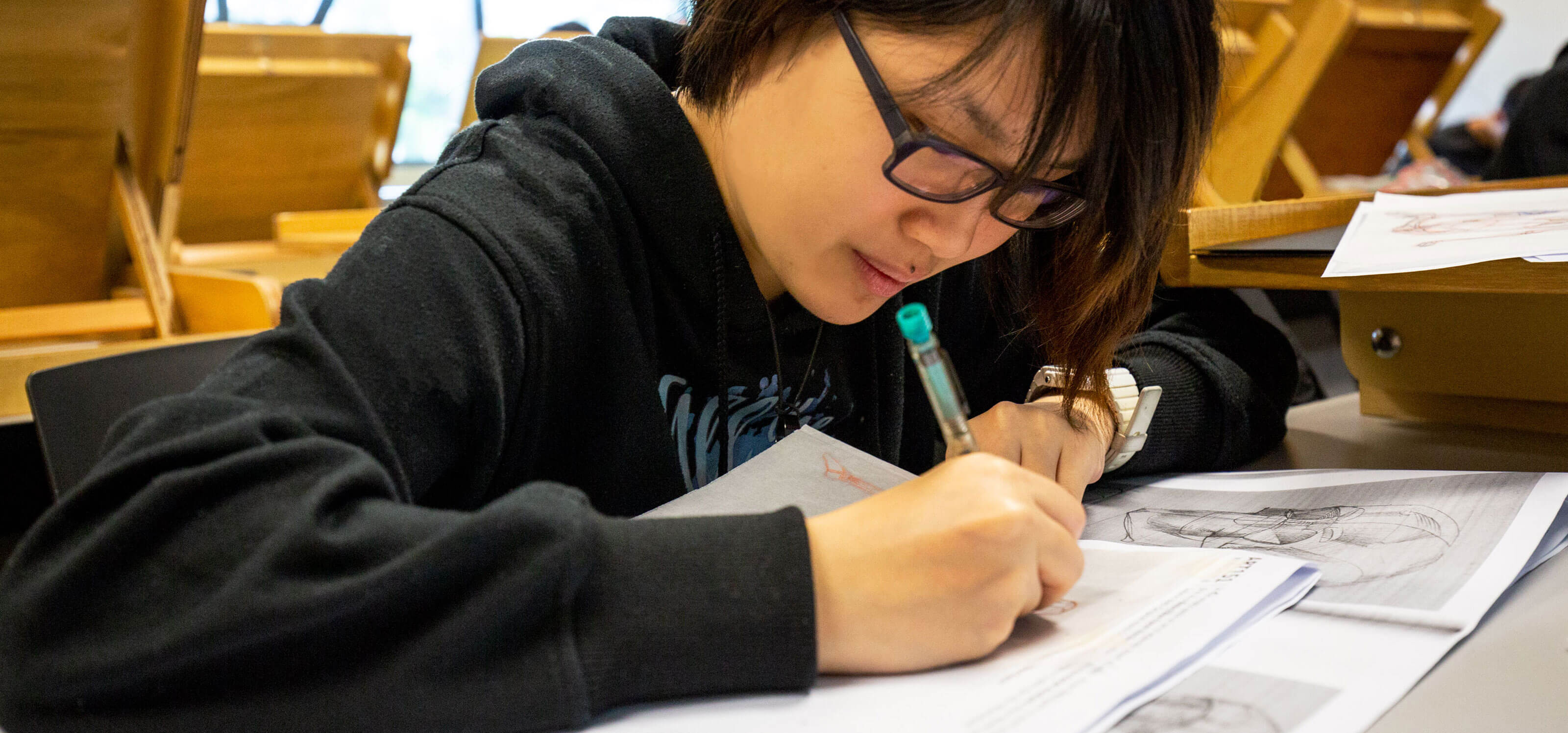 A DigiPen (Singapore) student draws with a pen on paper in a classroom