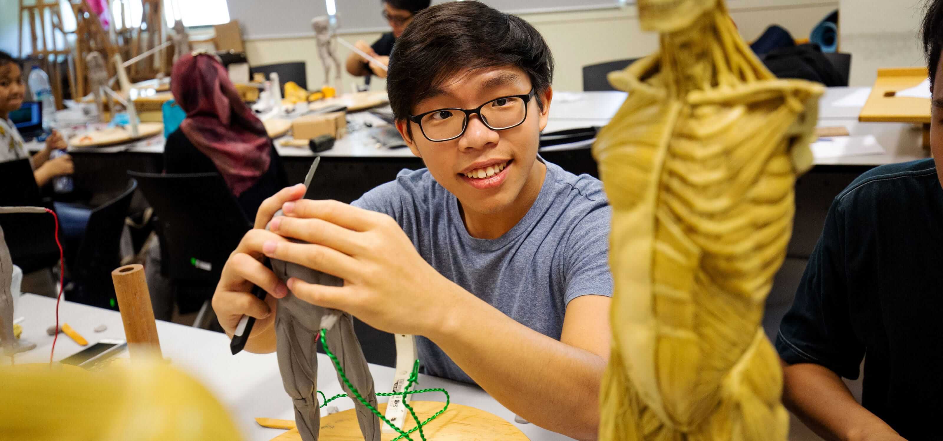 A DigiPen (Singapore) student smiles for the camera as he works on a sculpture of a human figure