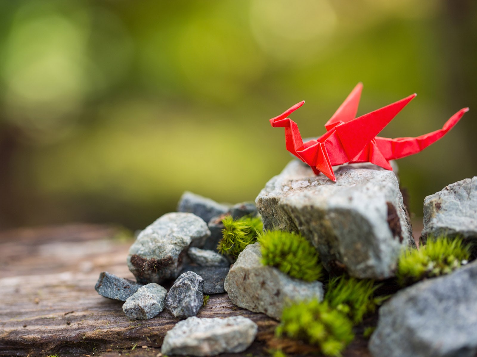 A dragon crafted from red origami paper sitting on a mossy rock