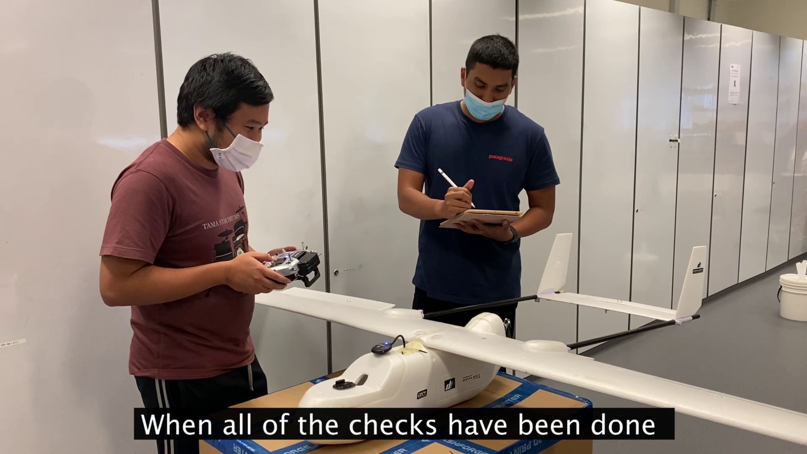 Two students stand next to a white drone while working on it