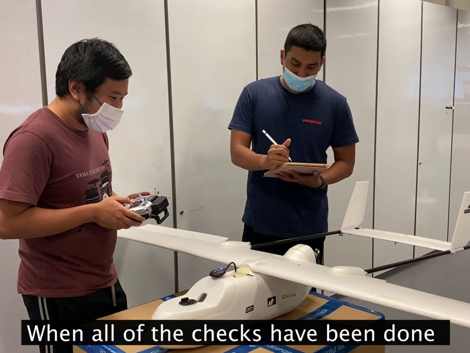Two students stand next to a white drone while working on it