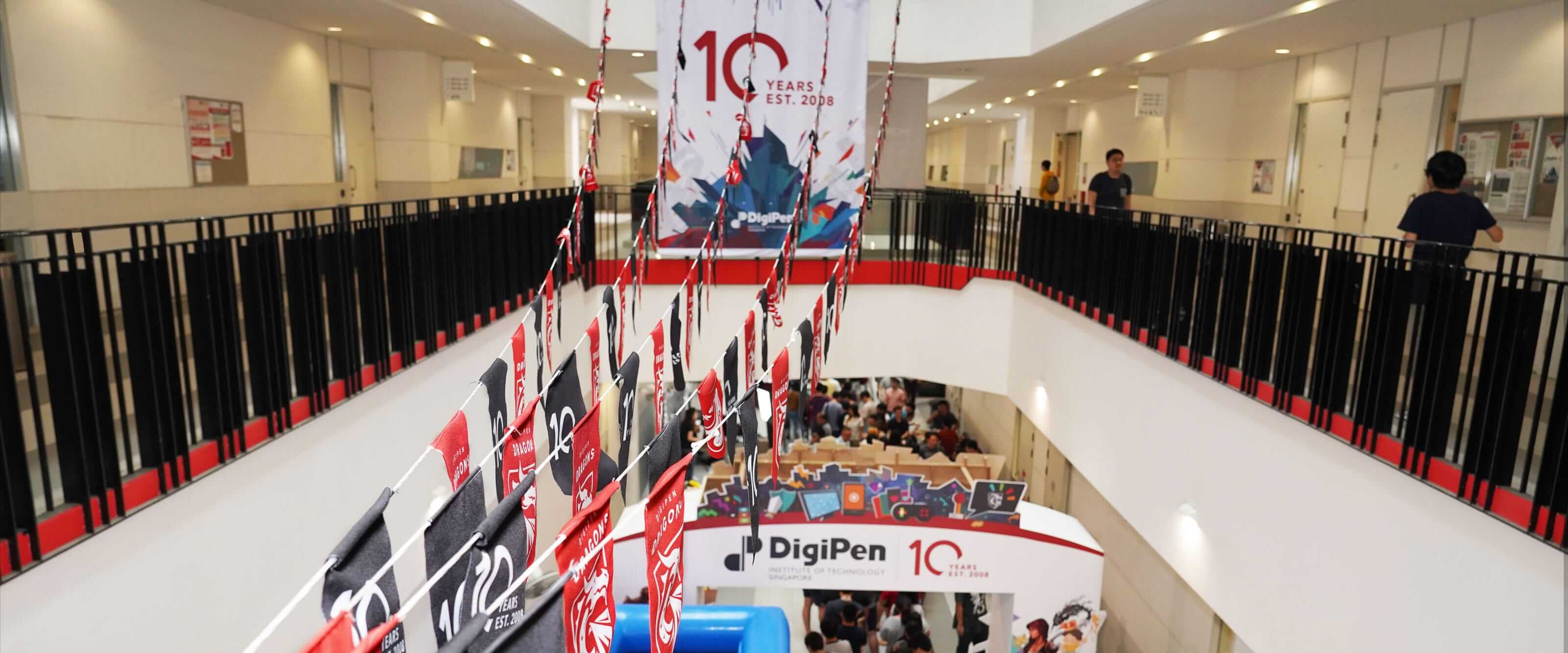 School banners and pennants hang in a multi-level, interior atrium area while a celebration takes place on the ground floor.