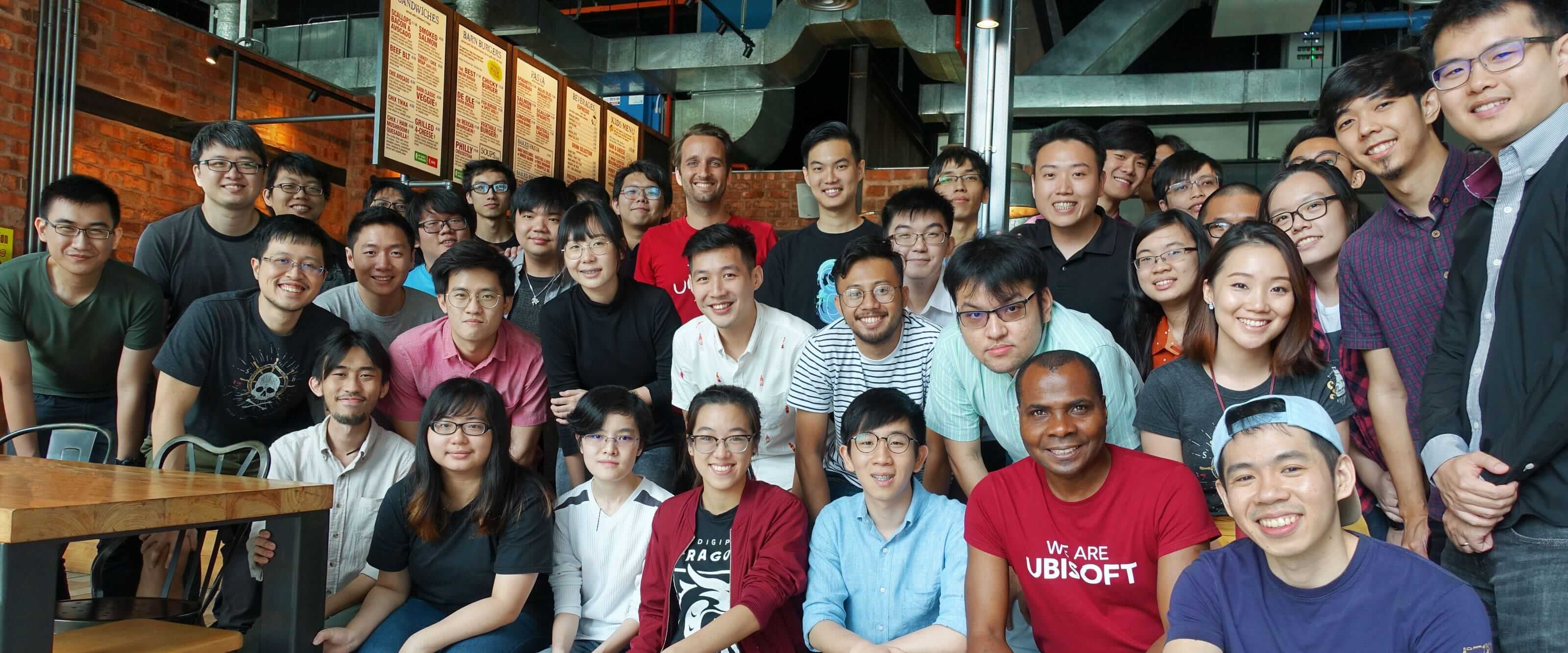 Dozens of people, while kneeling and standing, pose and smile for a photo inside a restaurant.