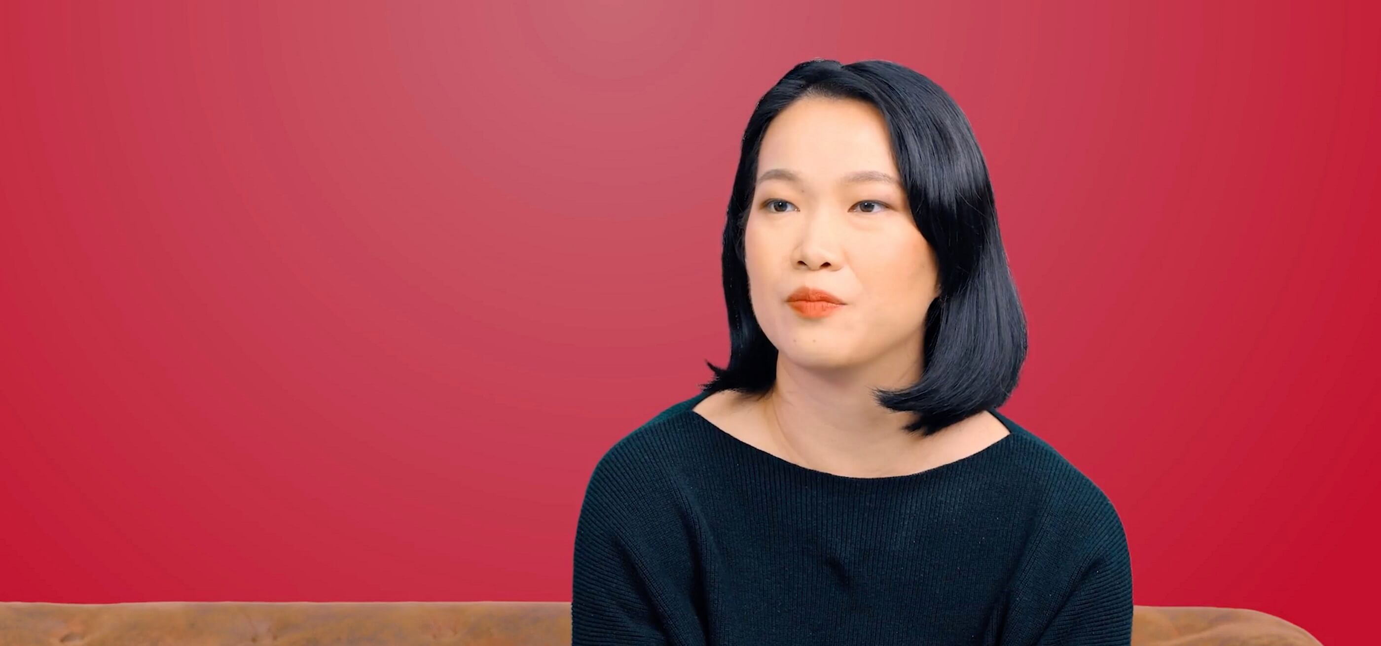 A DigiPen (Singapore) graduate sits in front of a red background and looks ahead