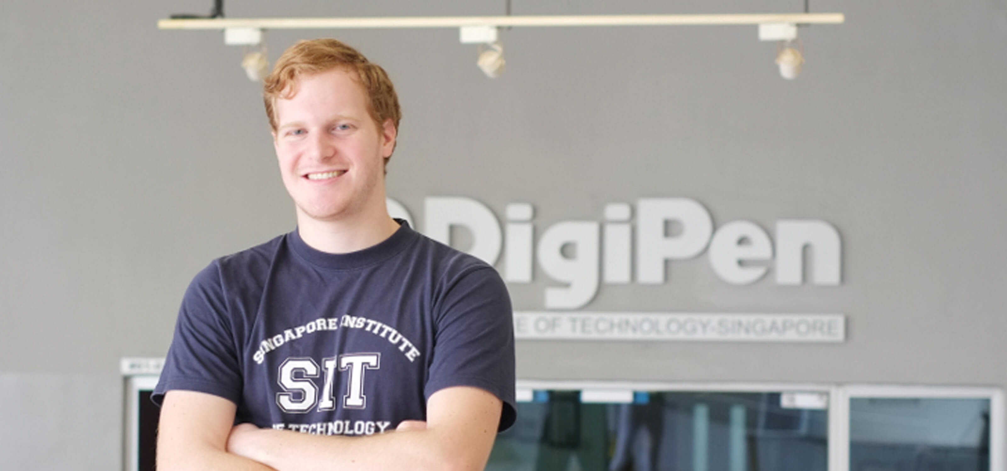 RTIS student Alan Miller poses for a photo arms crossed in front of a building. DigiPen logo is on the building behind him.