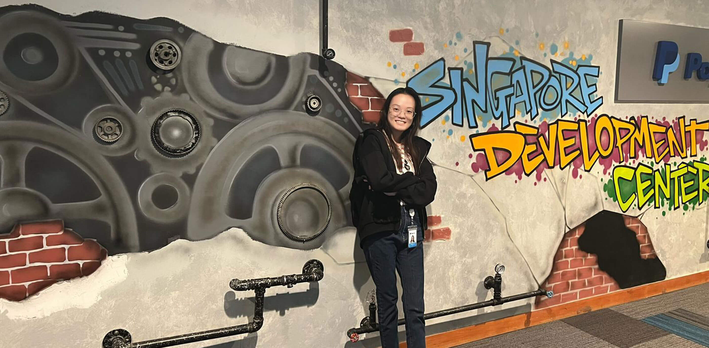 Alumna Jobelle Lim stands against a wall with stylized graffiti that reads 'Singapore Development Center'