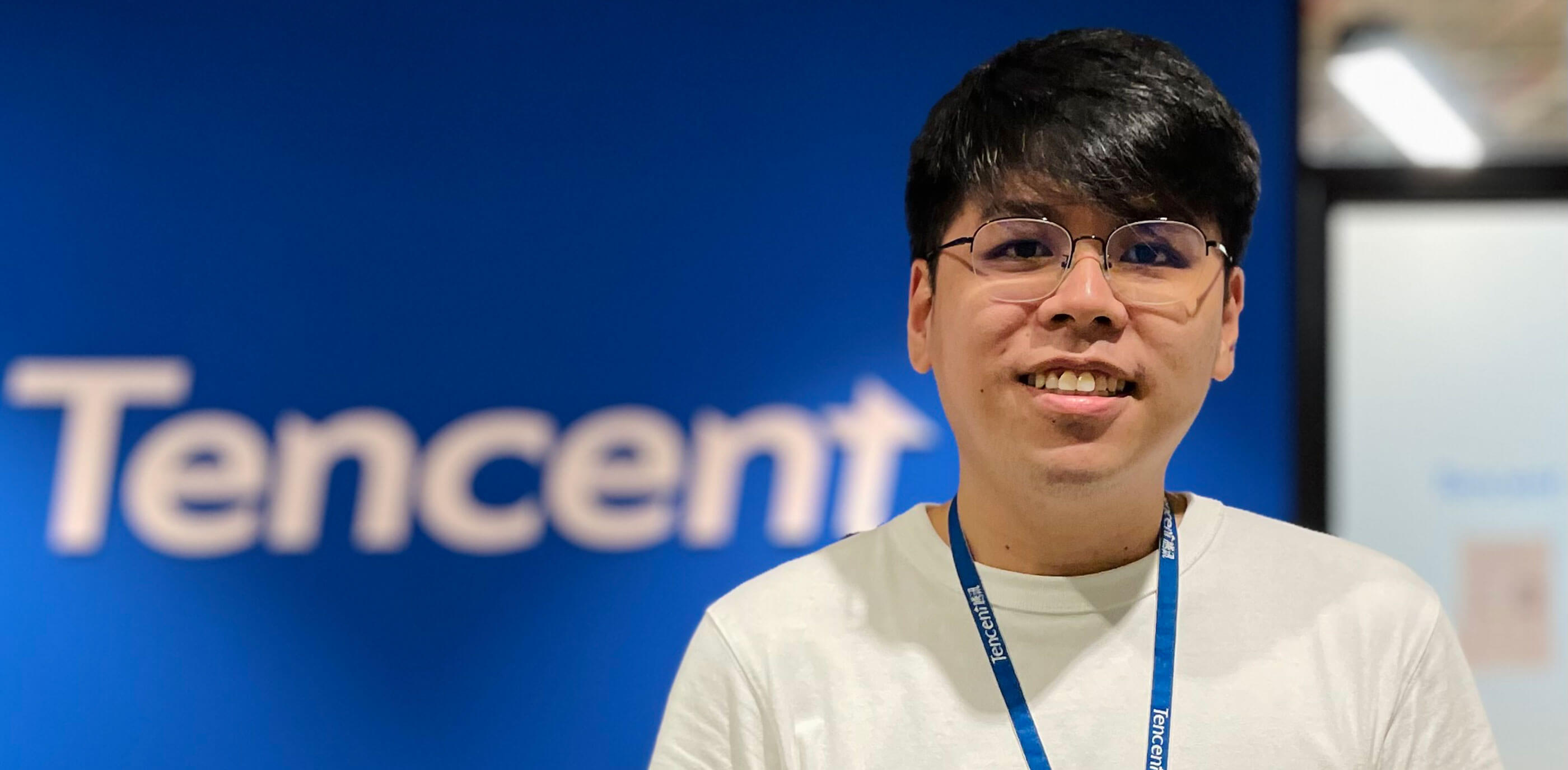 Alumni Mandl Cho stands in front of a blue wall with the Tencent logo on it