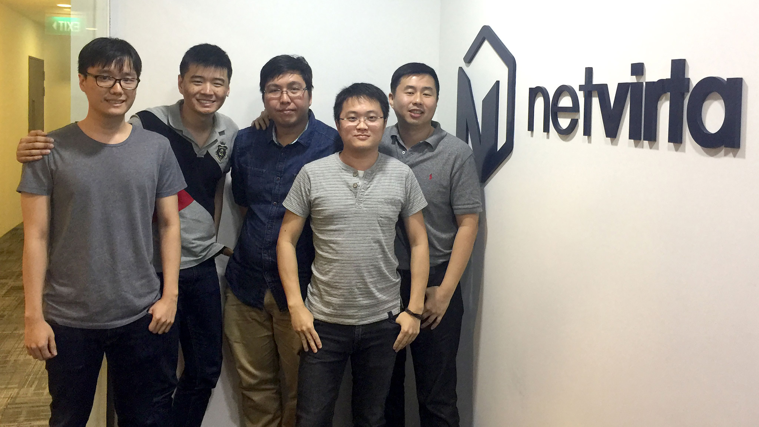 A group of DigiPen Singapore alumni pose next to the logo of Boston-based startup company NetVirta