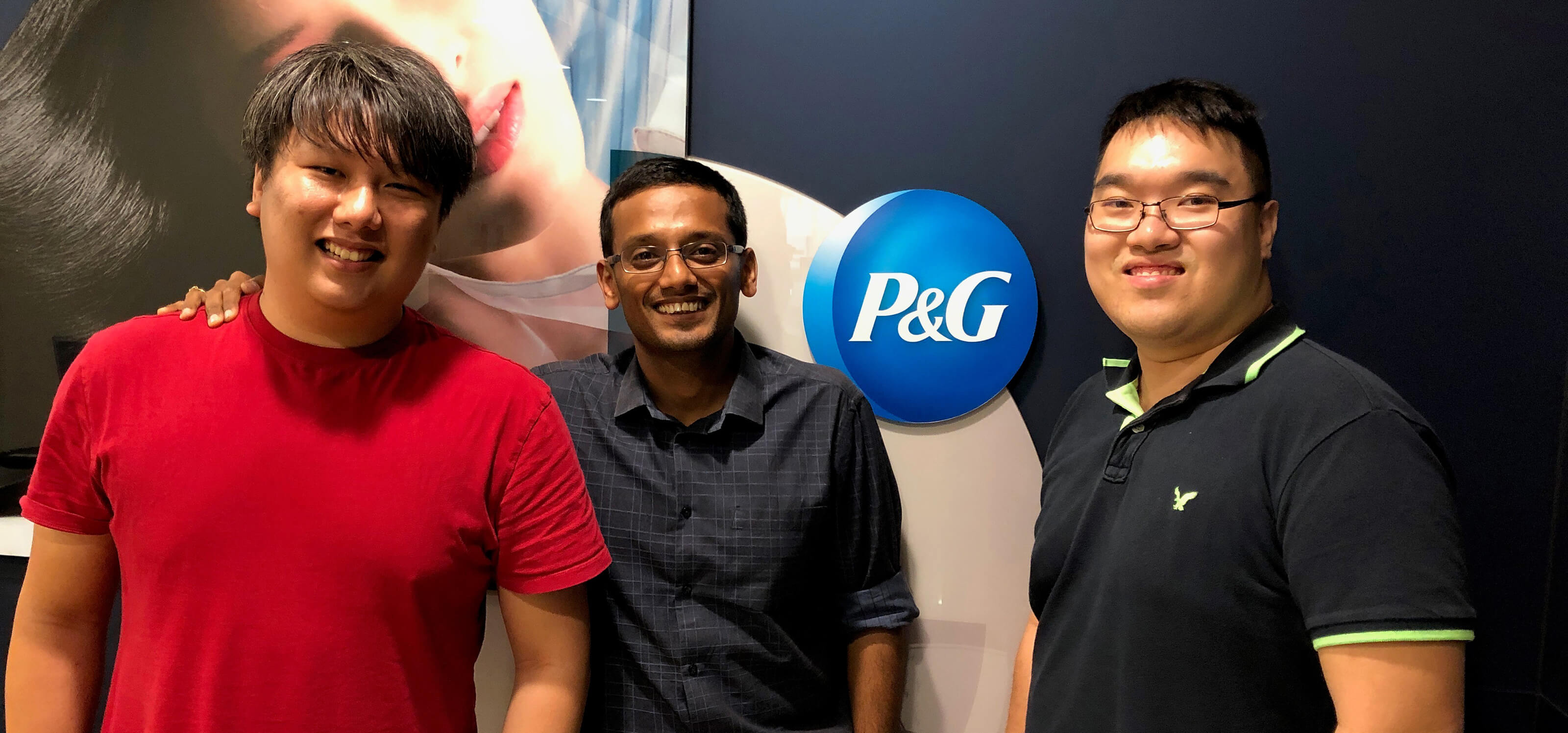 Two SIT-DigiPen (Singapore) graduates stand in front of the Procter &amp; Gamble company logo