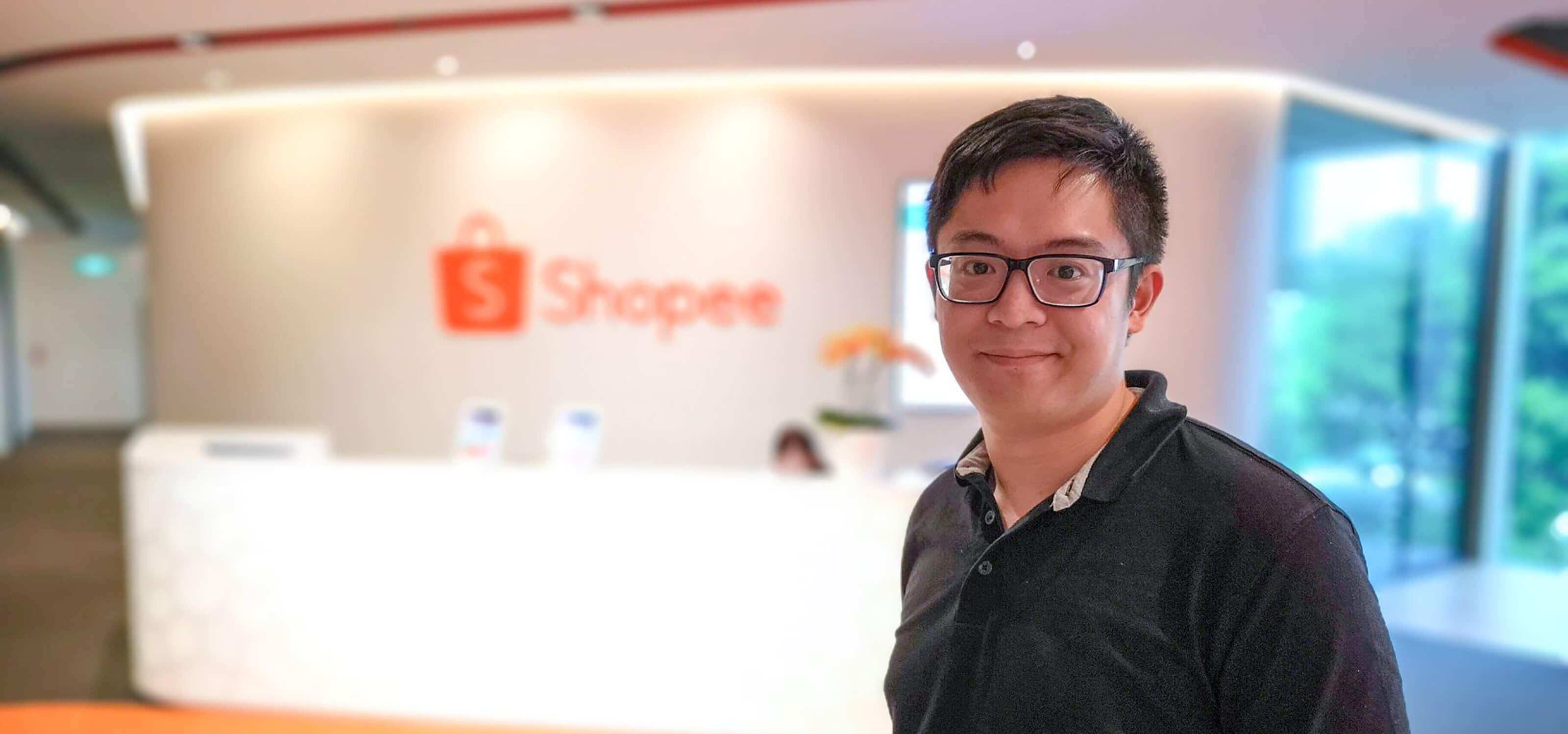 DigiPen (Singapore) alumnus Chester Liew stands in front of a wall adorned with the Shopee logo