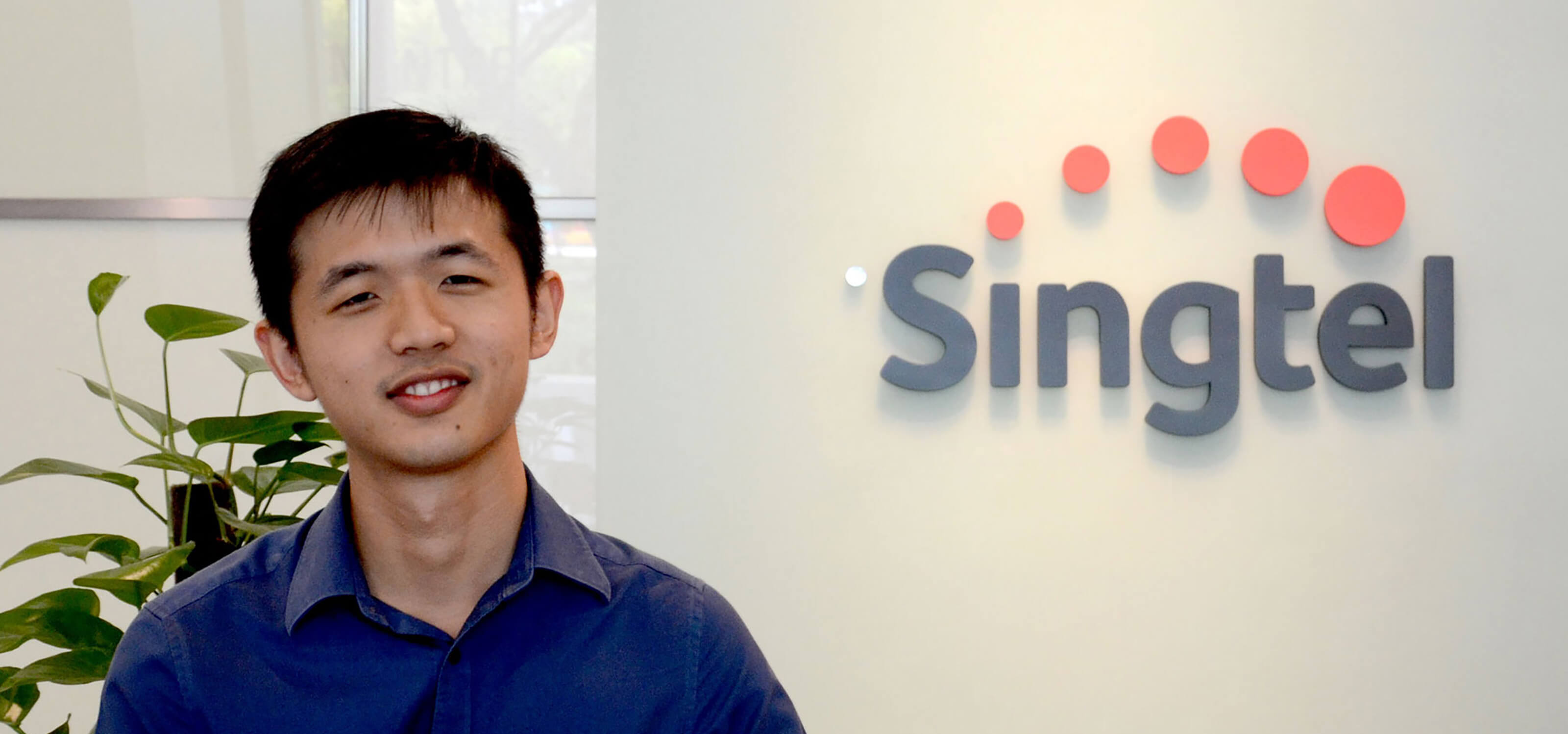 DigiPen (Singapore) BA in Game Design alumnus Daryl Bong poses in front of the Singtel logo