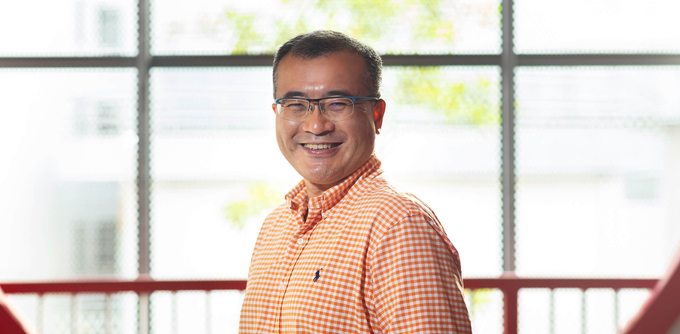 Dr Tang Lang smiles standing in front of a large window