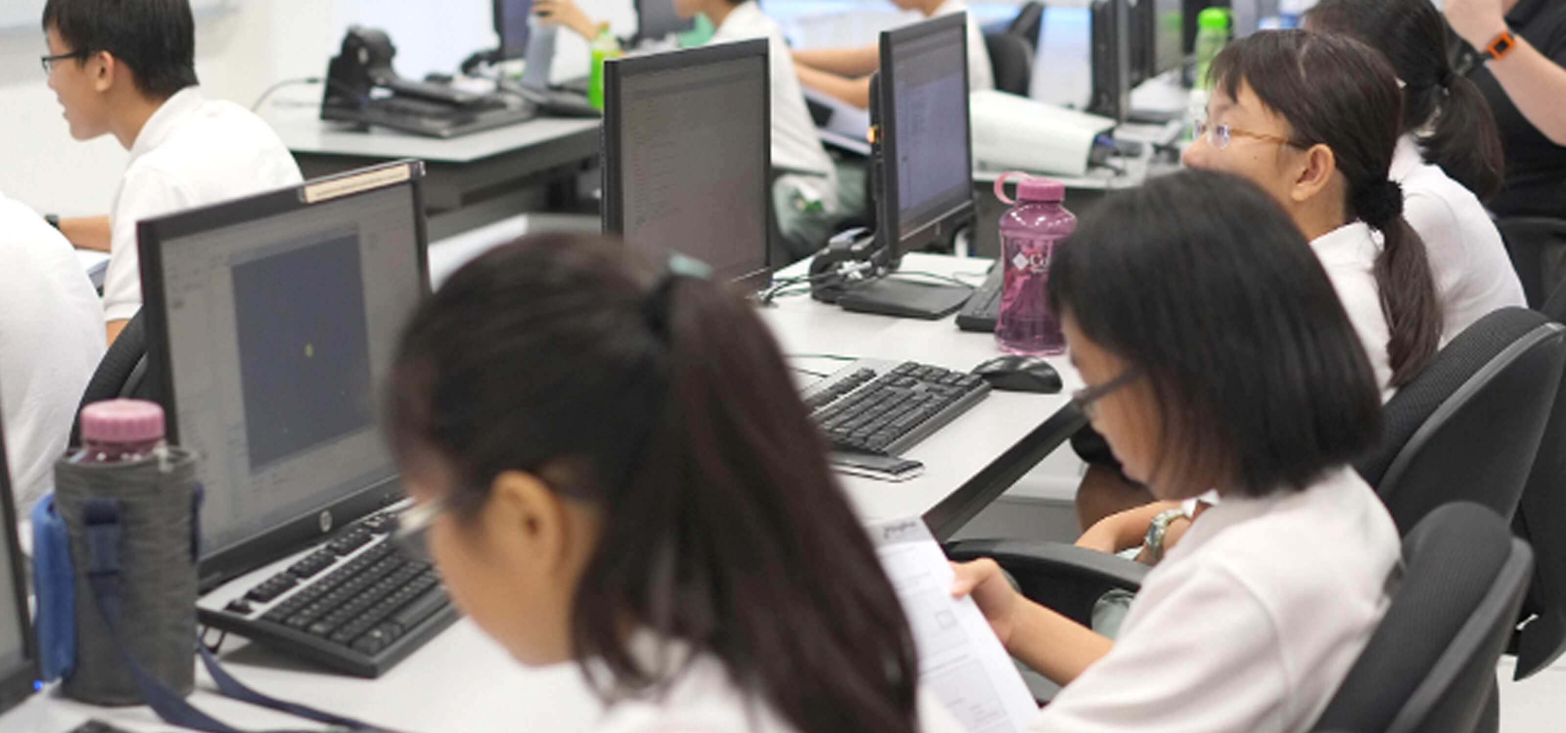 Students seen from over the shoulder, each sitting at a desk with a computer, working on different projects
