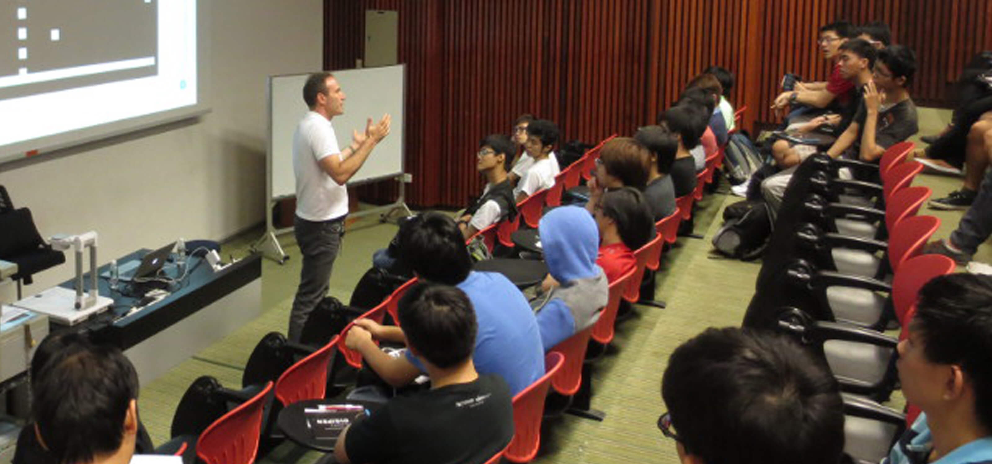 CTO Samir Abou Samra stands speaks to students in a lecture hall with a projection screen behind him