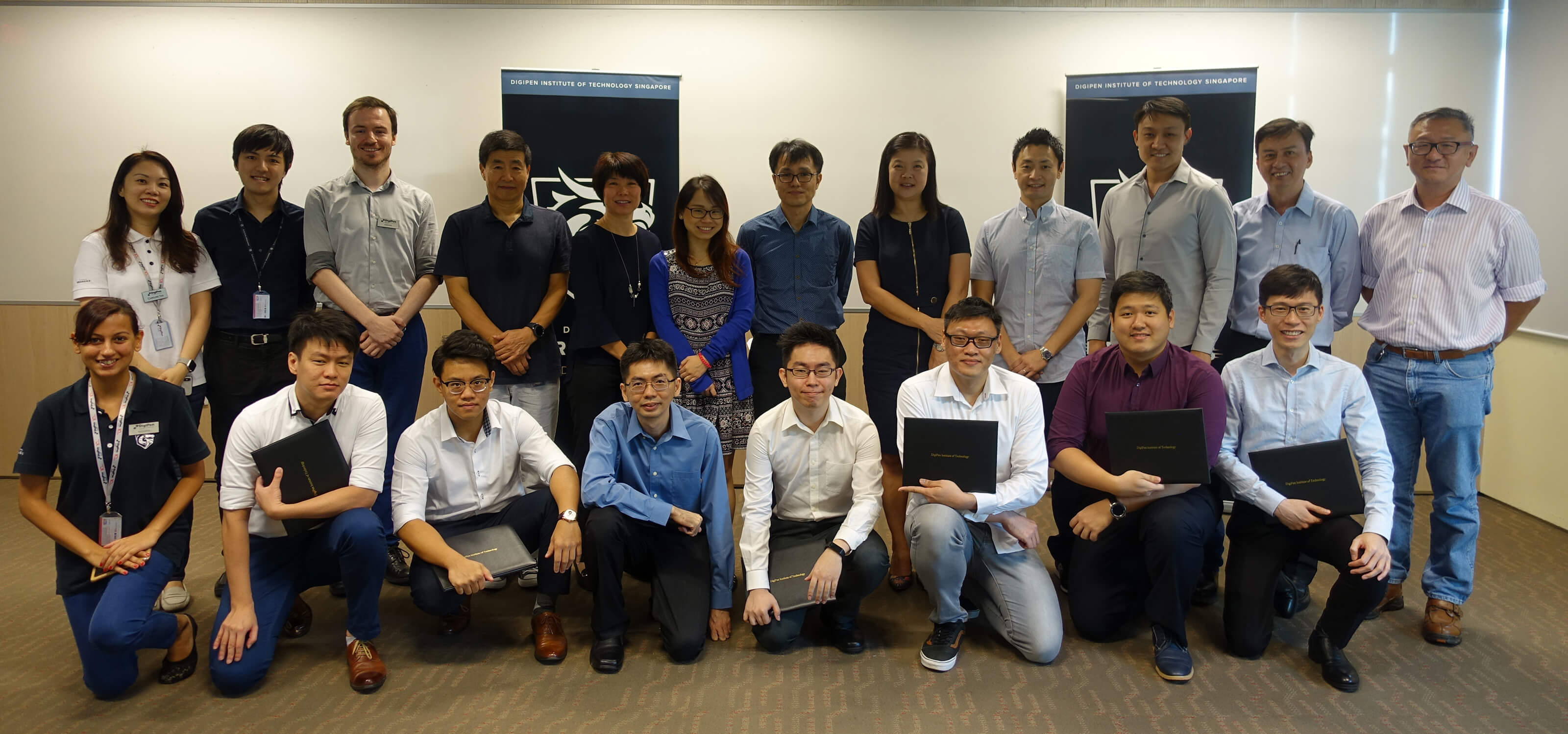 Group photo of 20 people lined up in two rows, including seven CE program graduates in front, holding their diplomas.