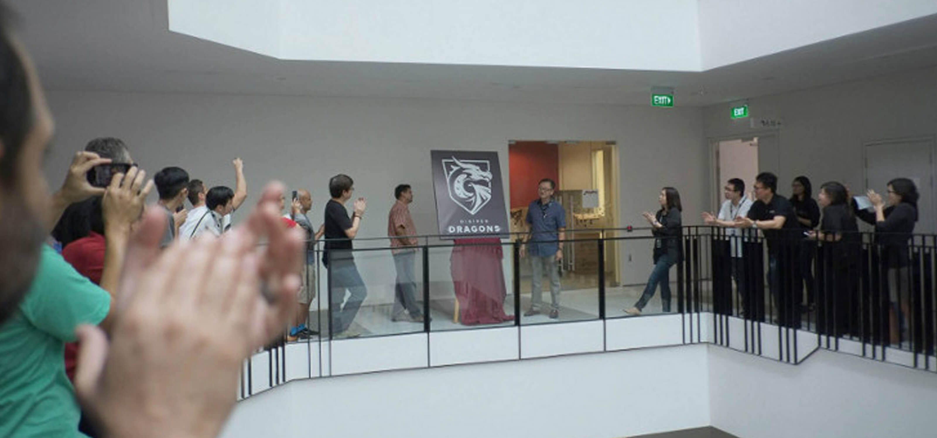 People on the second floor applaud the unveiling of a poster depicting the DigiPen Dragons logo