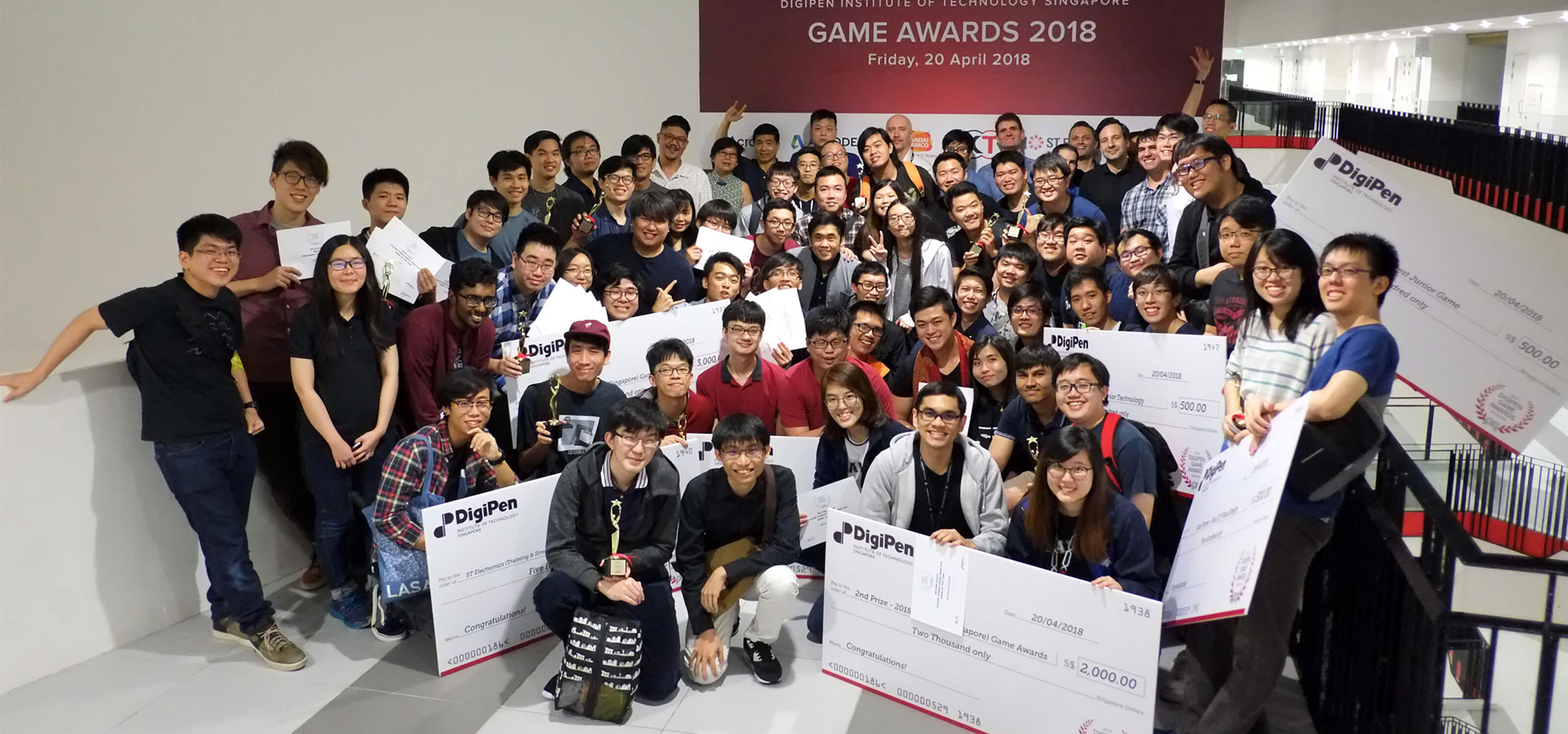 Participants in the DigiPen (Singapore) Game and Animation Awards pose, with award-winners holding giant novelty checks up front