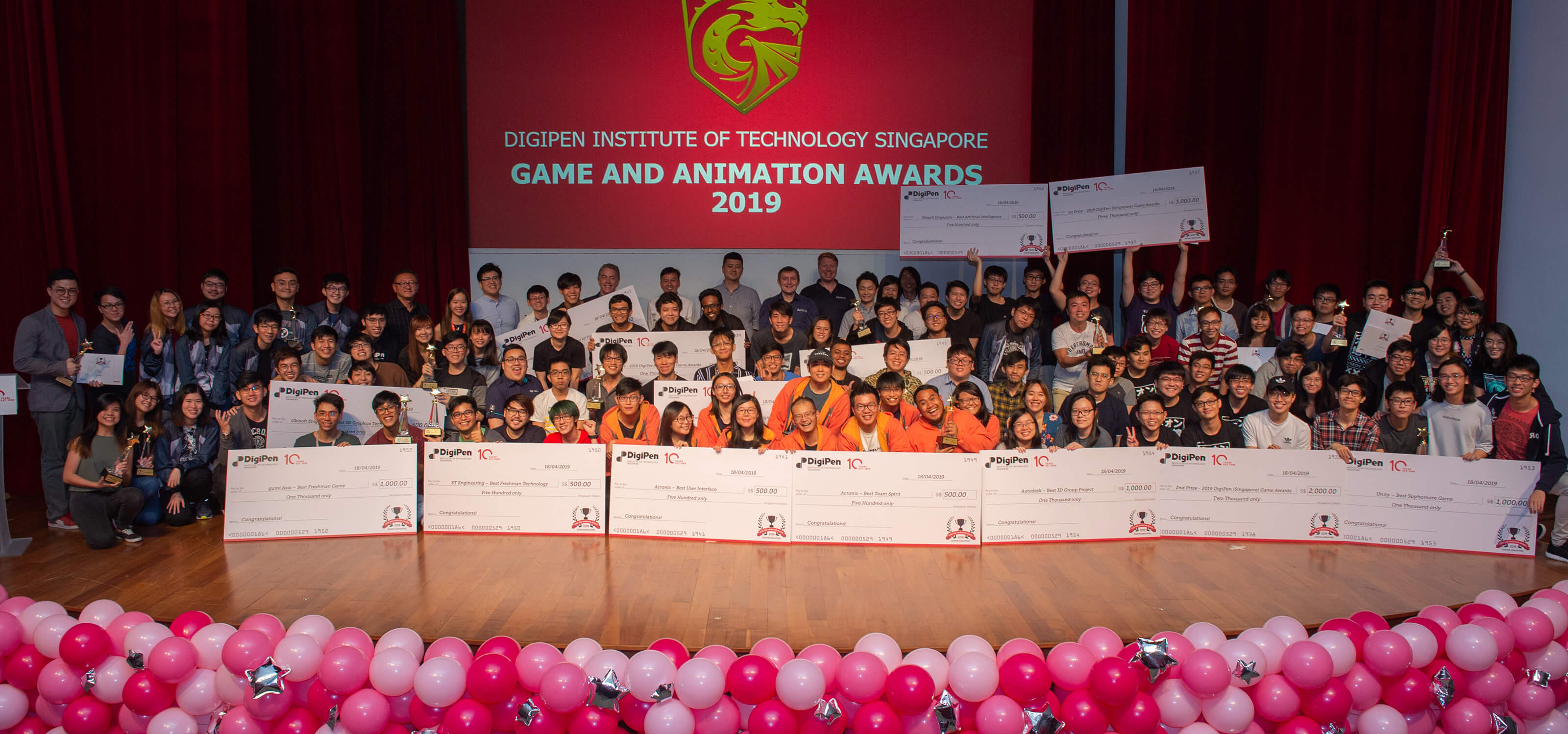 Four rows of students line up on stage to display their giant prize checks during the 2019 DigiPen Game and Animation Awards ceremony.