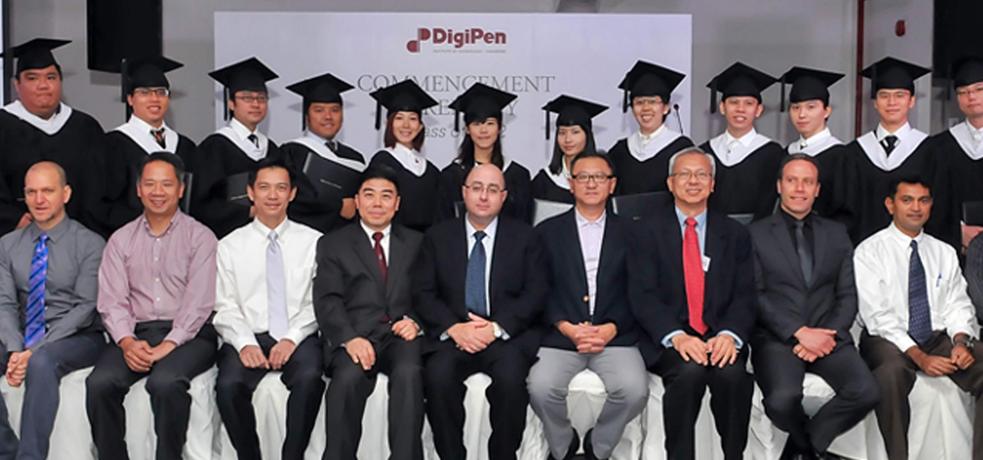 12 DigiPen (Singapore) graduates of the inaugural class pose in cap and gowns behind seated faculty and administration