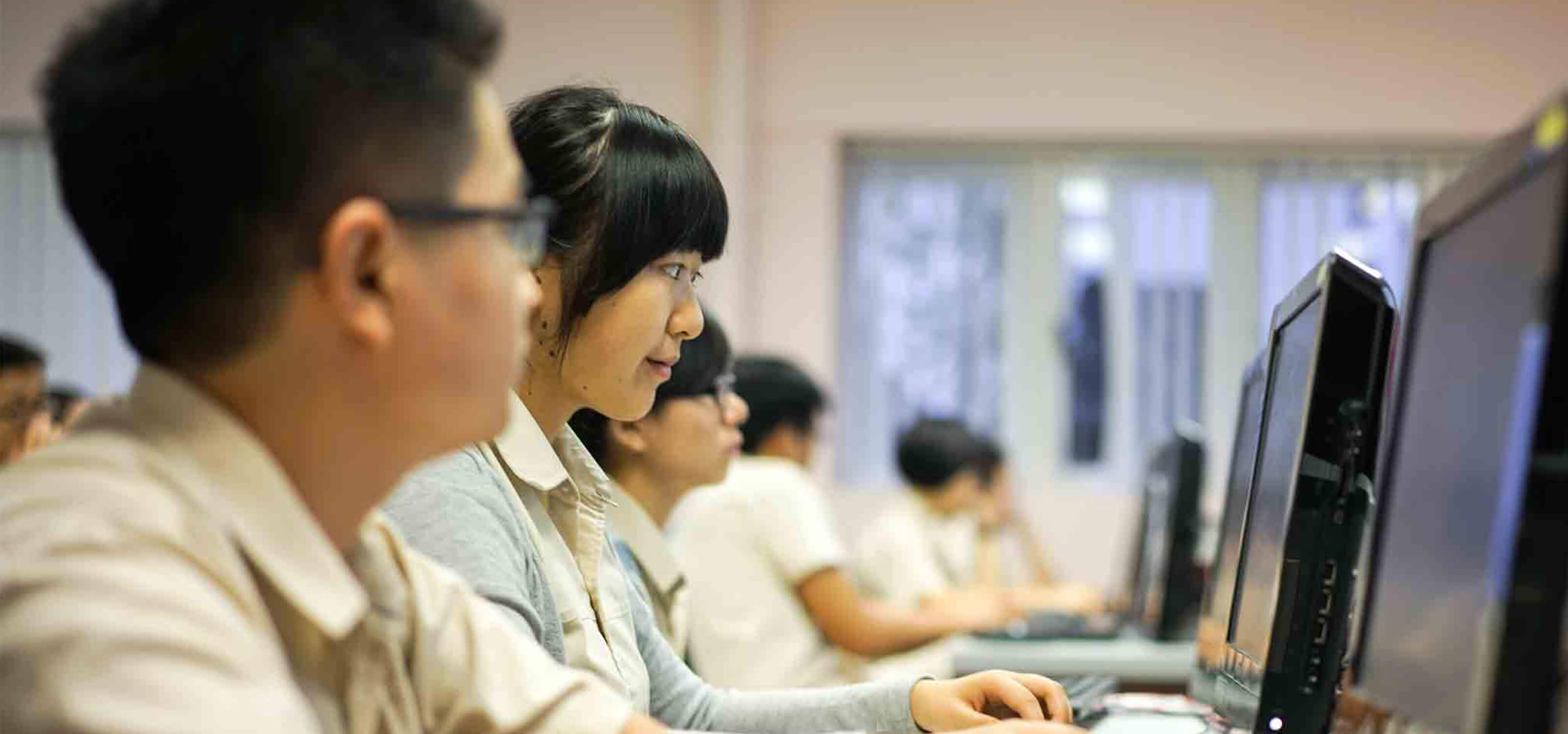 Students sit at a desk looking at a computer monitor while using a mouse and keyboard