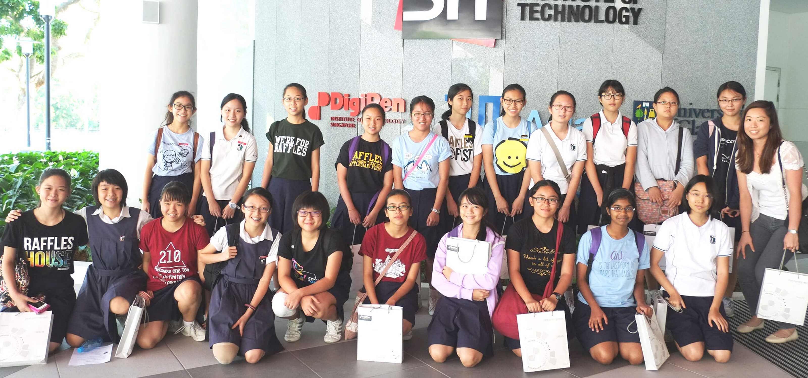 A group of schoolchildren pose for a picture in front of a building displaying the Singapore Institute of Technology logo