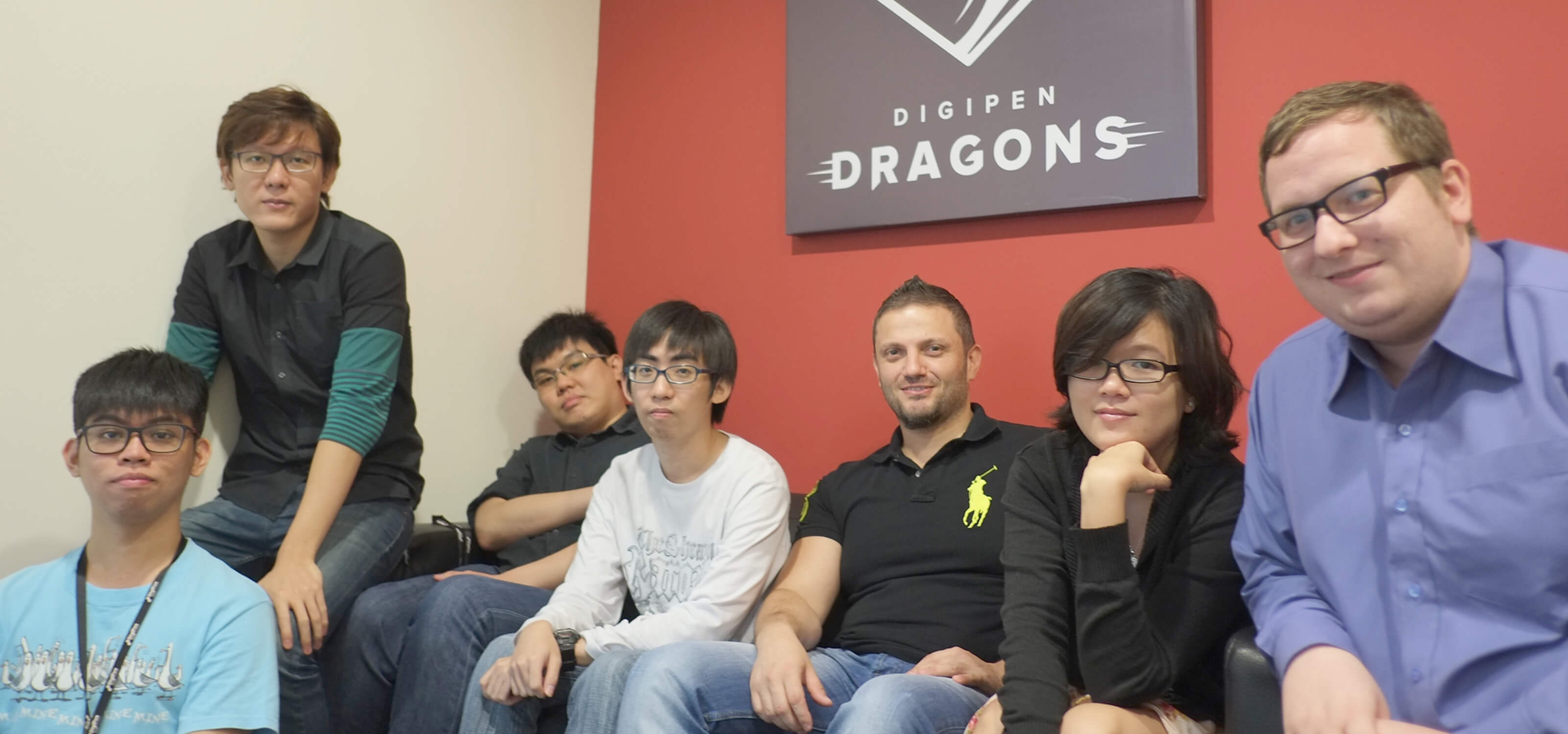 Members of the DigiPen (Singapore) Research and Development team sit at a couch below a poster of the DigiPen Dragons logo