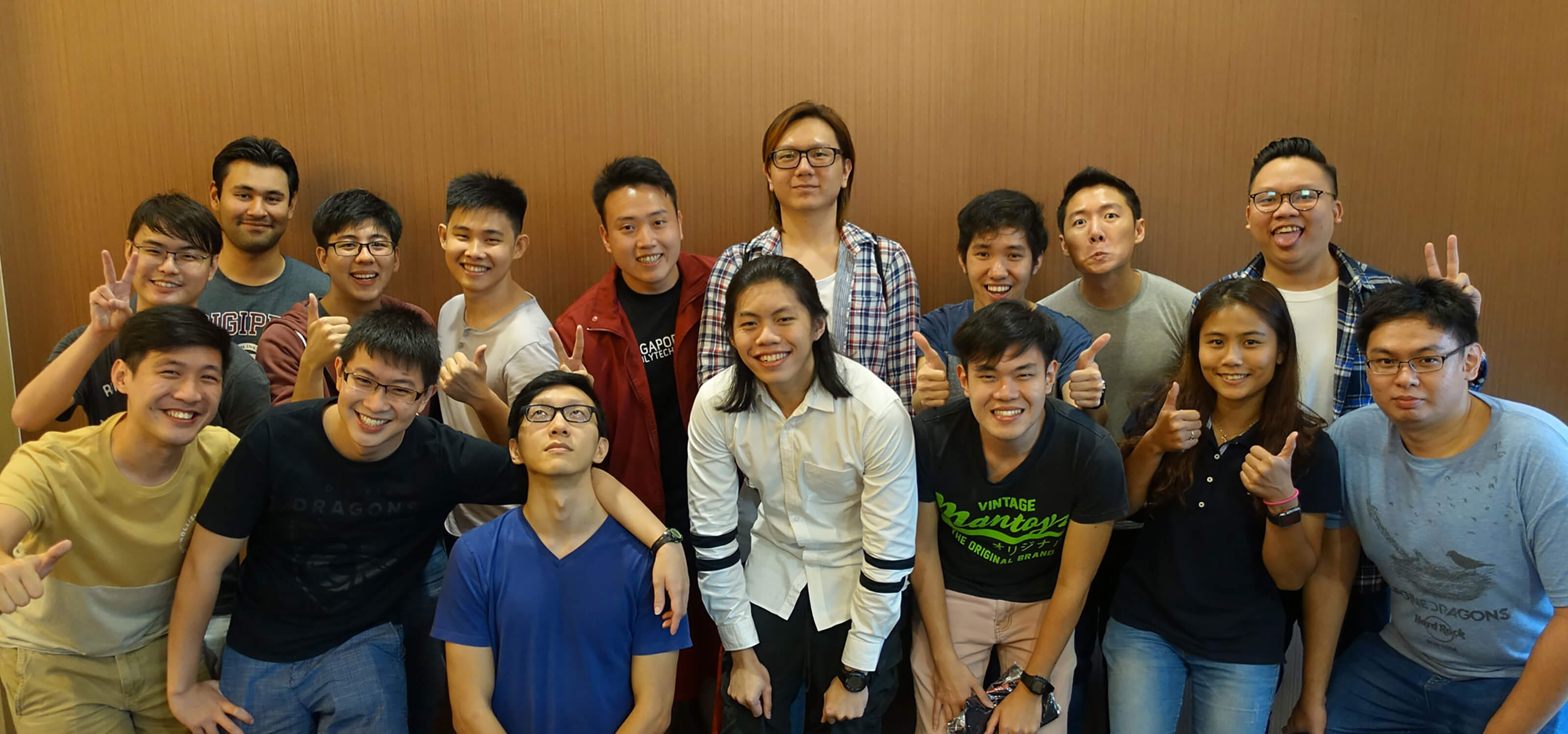 A large group of DigiPen (Singapore) Student Ambassadors smile for the camera, flashing peace and thumbs-up signs