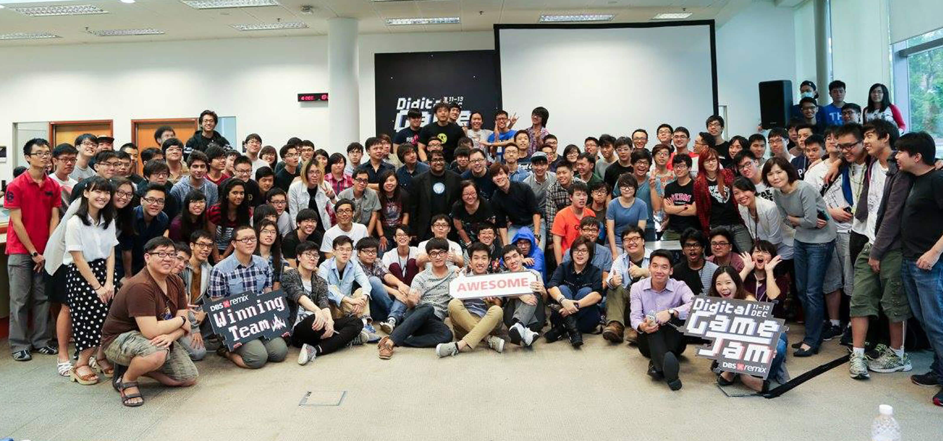 Dozens of students pose for a picture in an open, well-lit room; some hold Game Jam-related signs