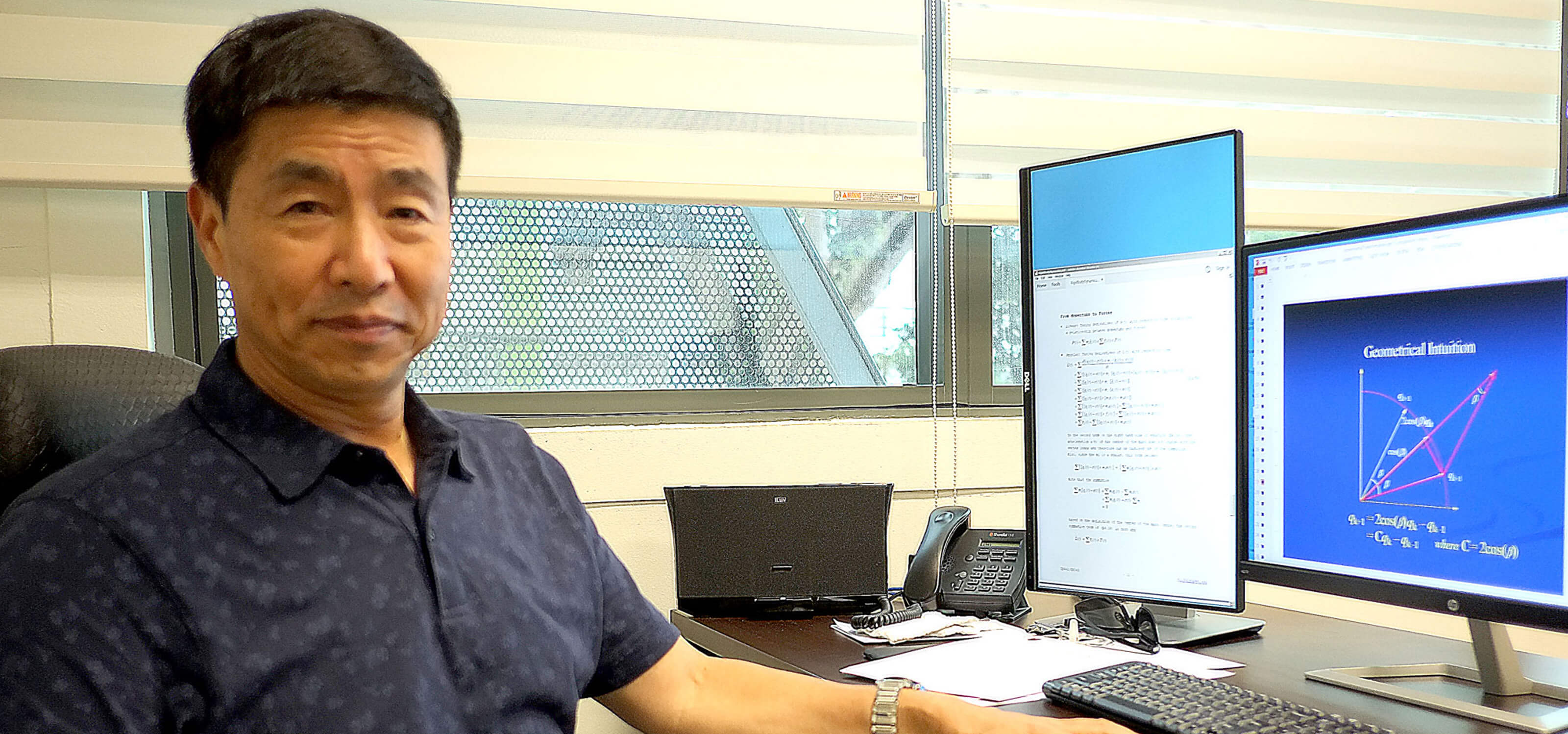 Dr. Xin Li poses for a photo at his desk which has one vertical and one horizontal monitor