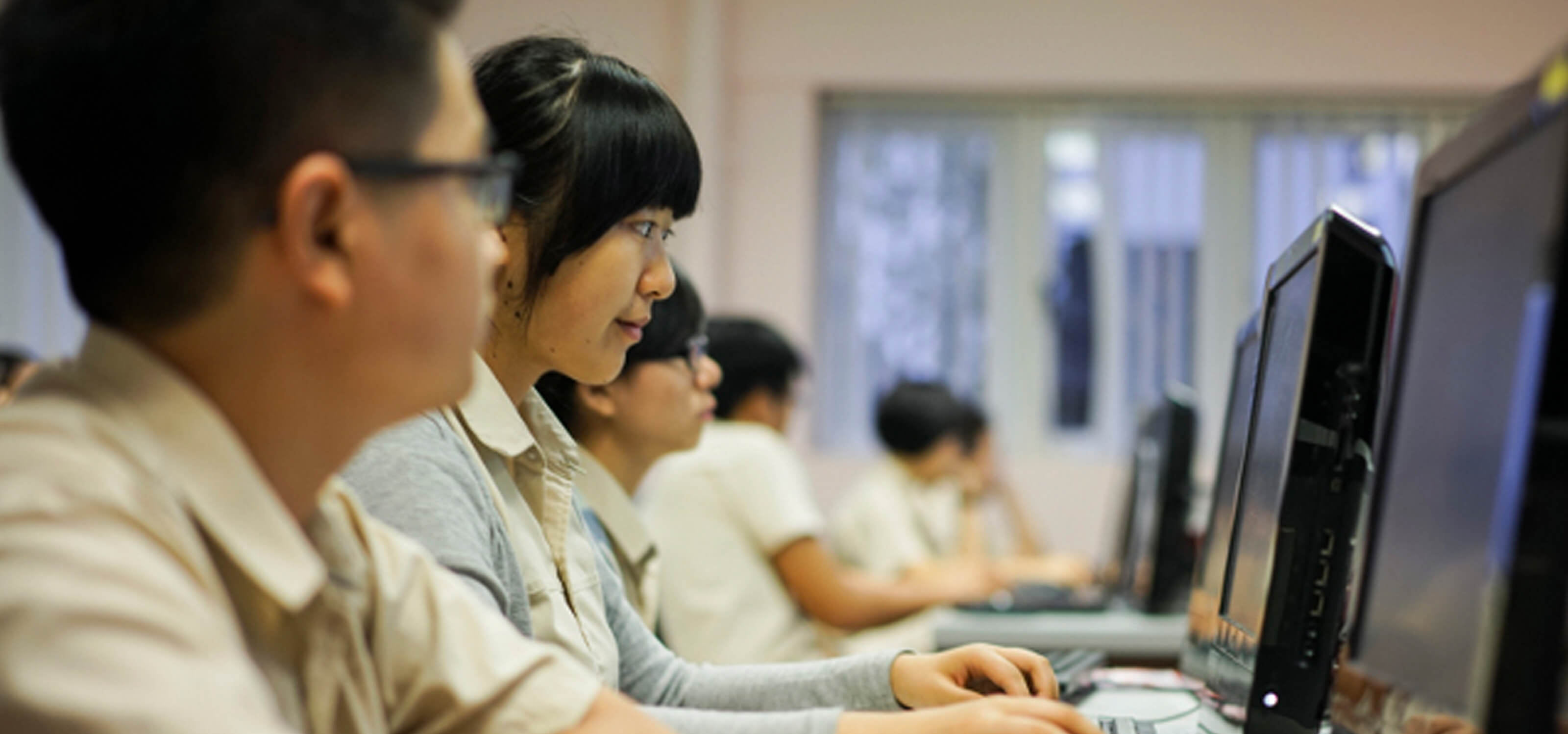 A student, seen from the side, looking at a computer monitor and working with a mouse and keyboard