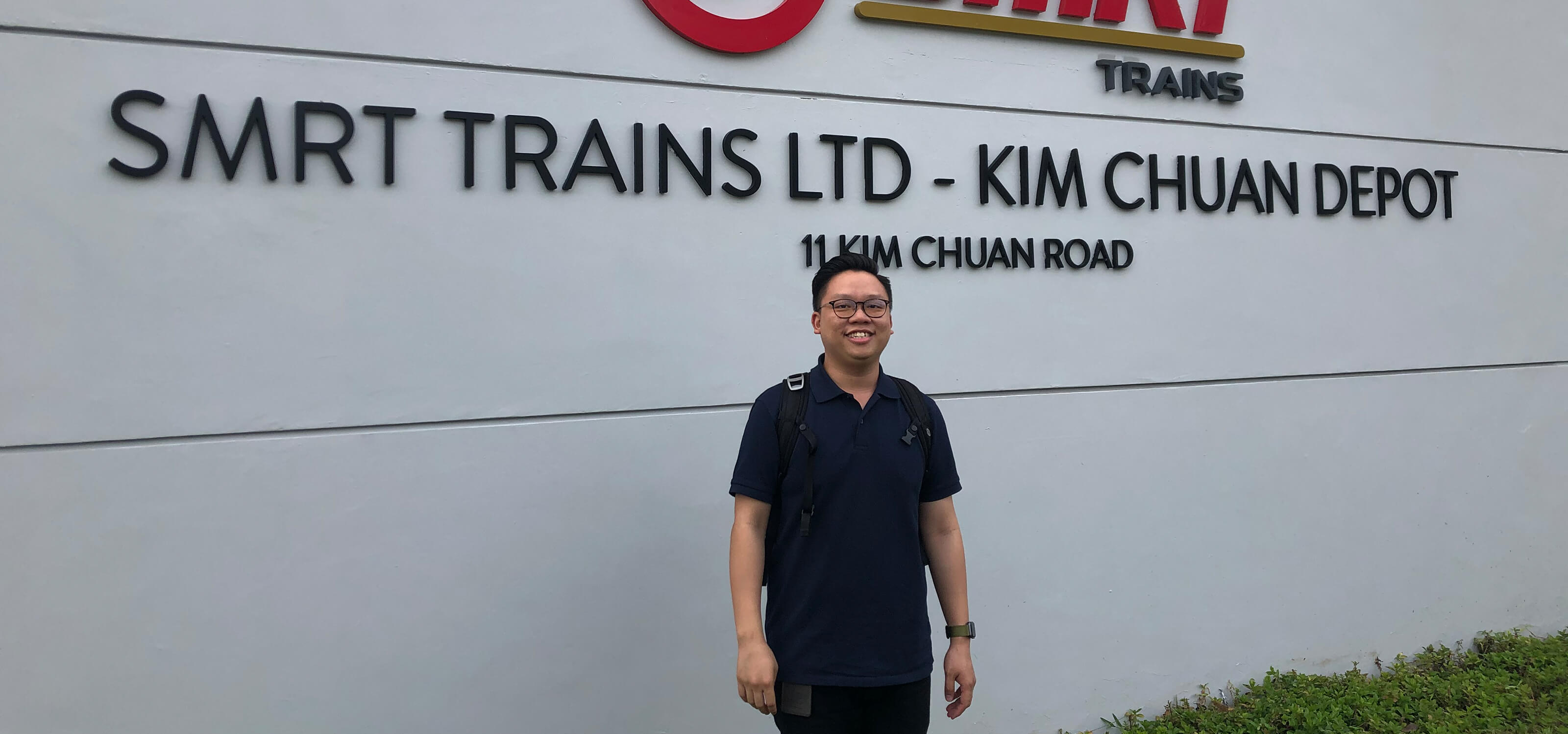 Samuel Tan stands in front of the ‘SMRT Trains Ltd. - Kim Chuan Depot” sign.