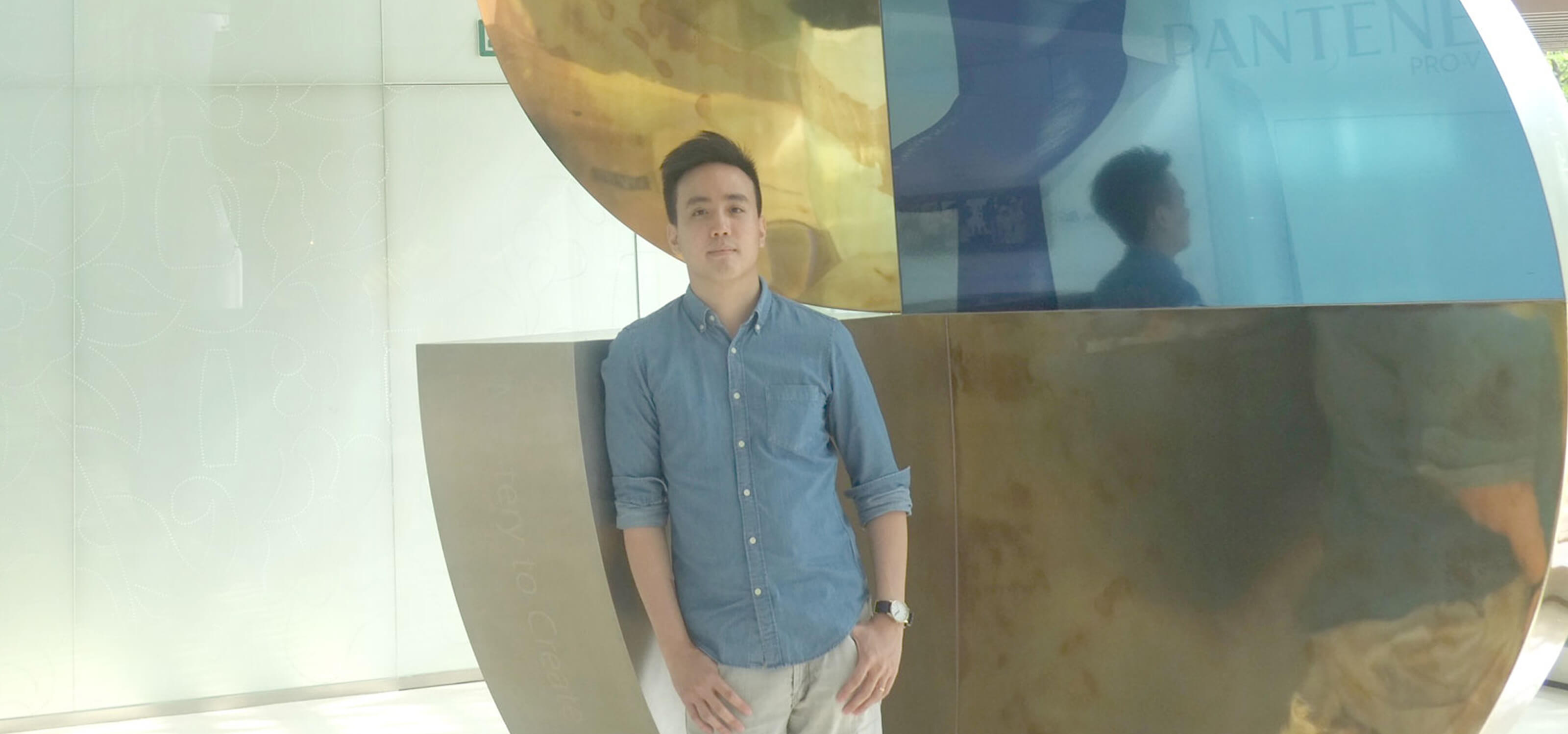 Graduate Larry Low Yun Long stands in the Proctor &amp; Gamble lobby next to a metal statuary