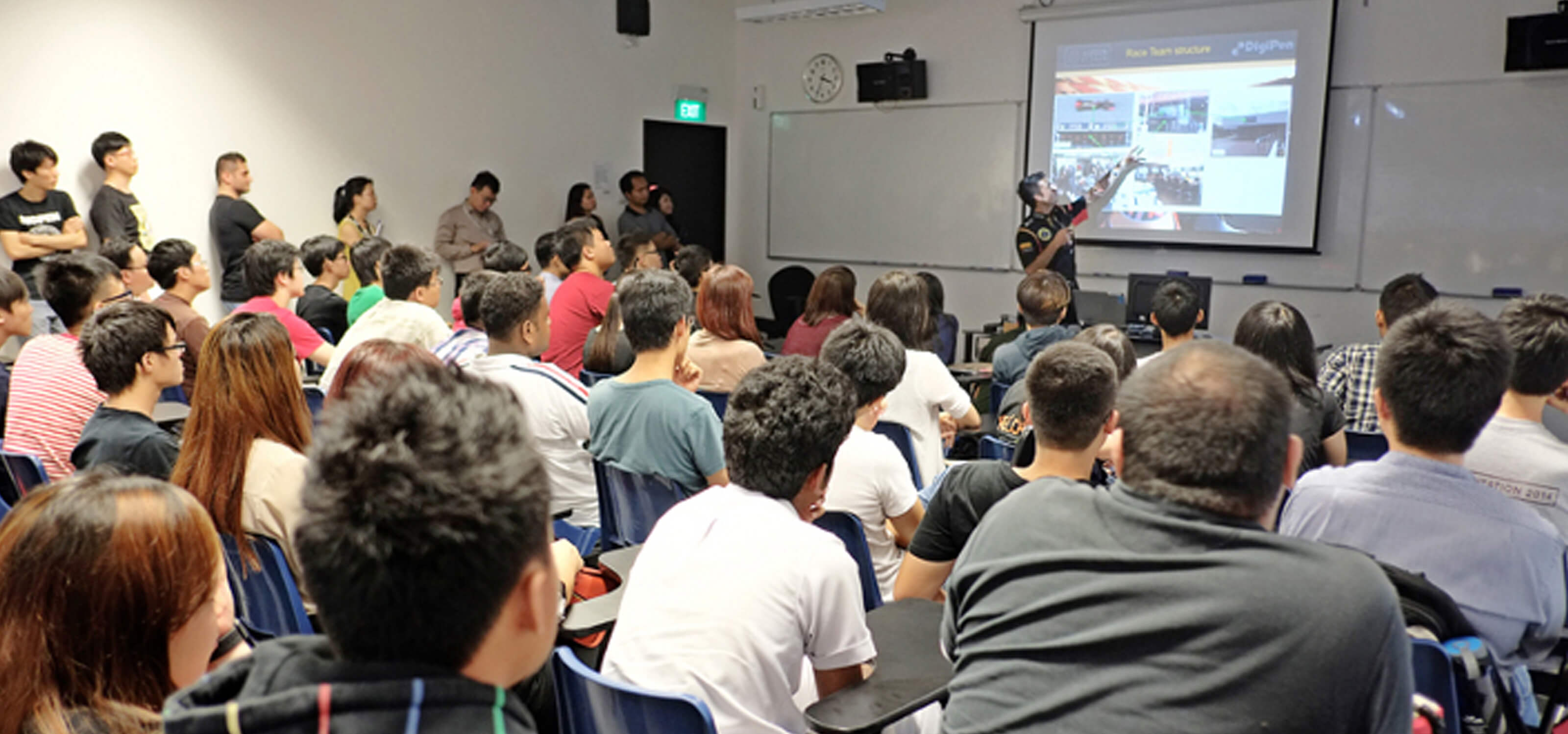 Lotus F1 team member points to a projection screen in front of a room full of audience members