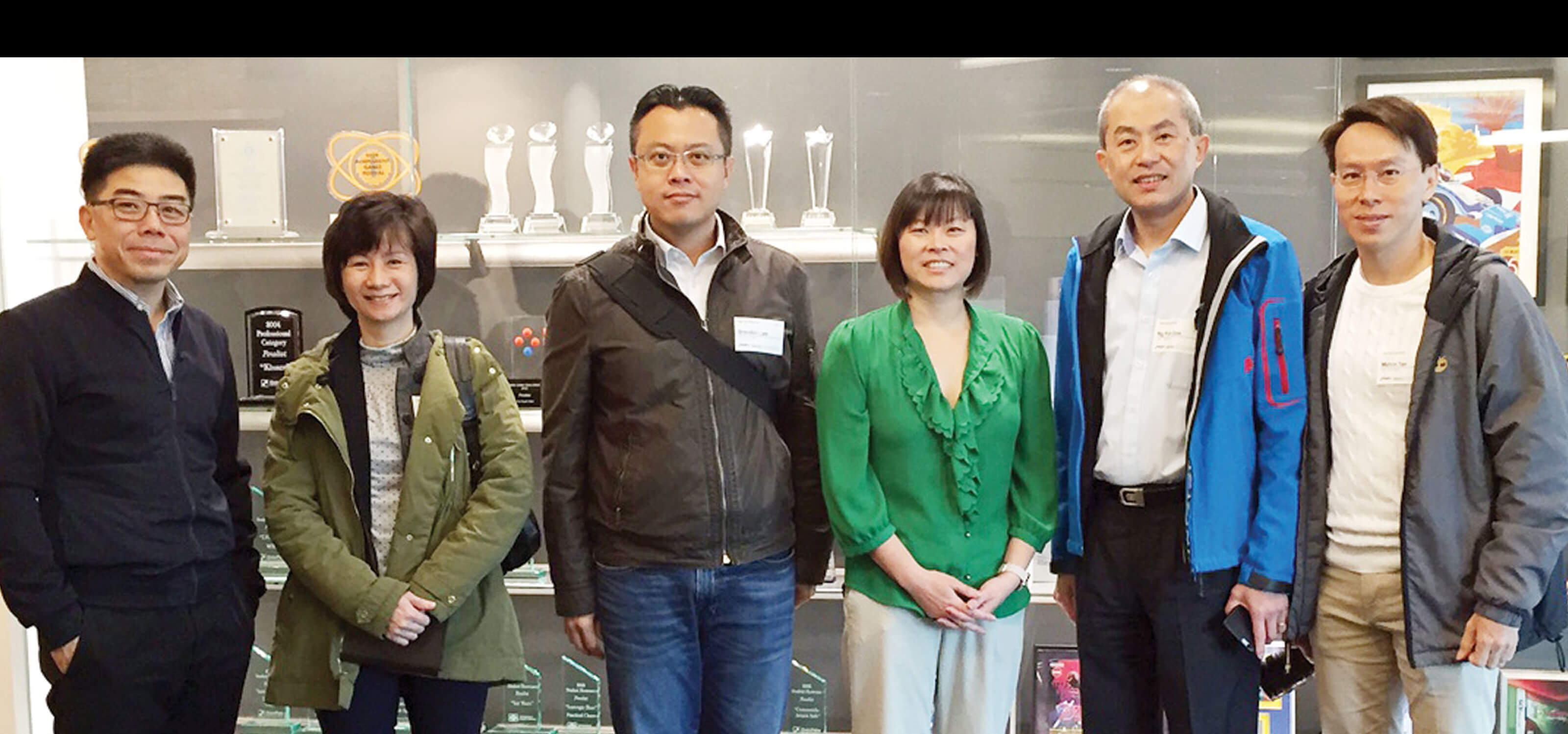 Visitors from Ngee Ann Polytechnic pose for a photo in front of a display case of DigiPen awards and project posters