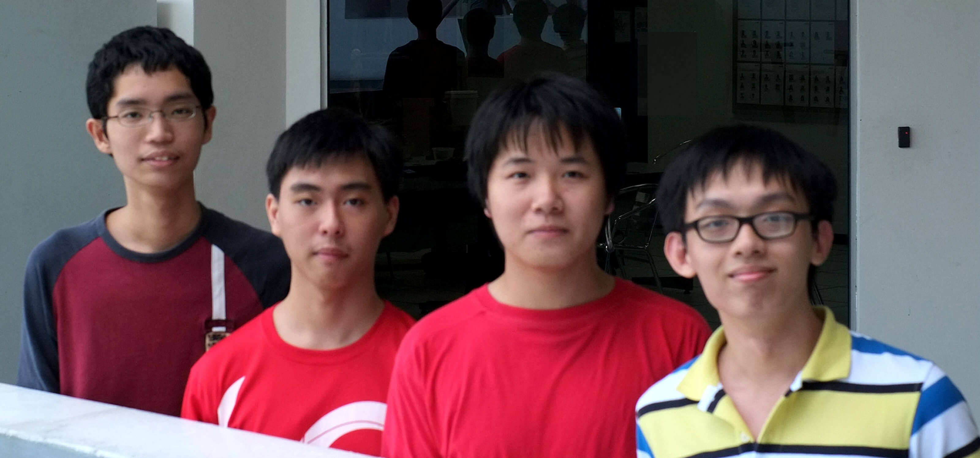 Four students pose for a photo behind a railing with an entrance to DigiPen (Singapore) behind them