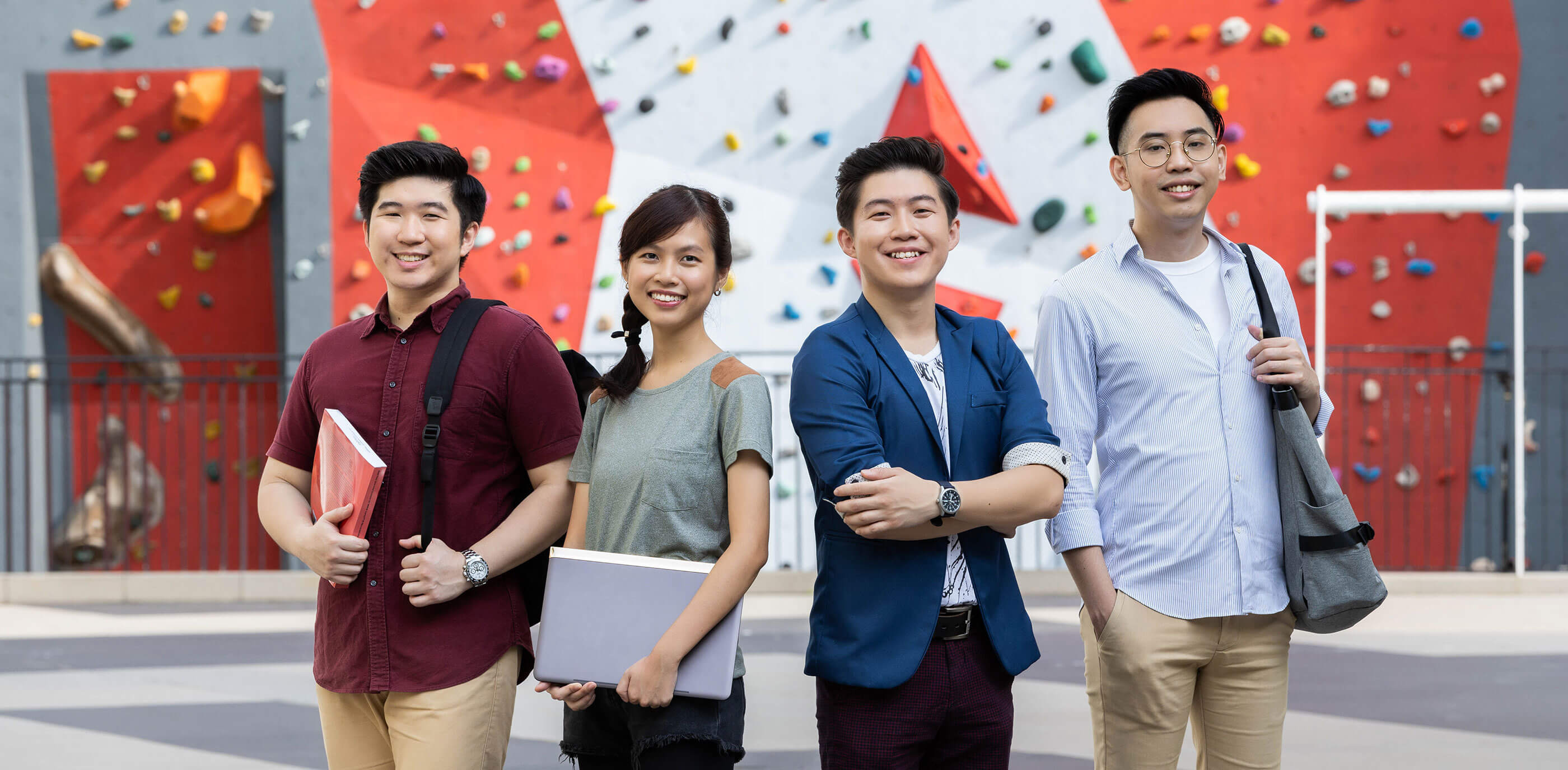 Four DigiPen (Singapore) students pose in front of a rock climbing wall