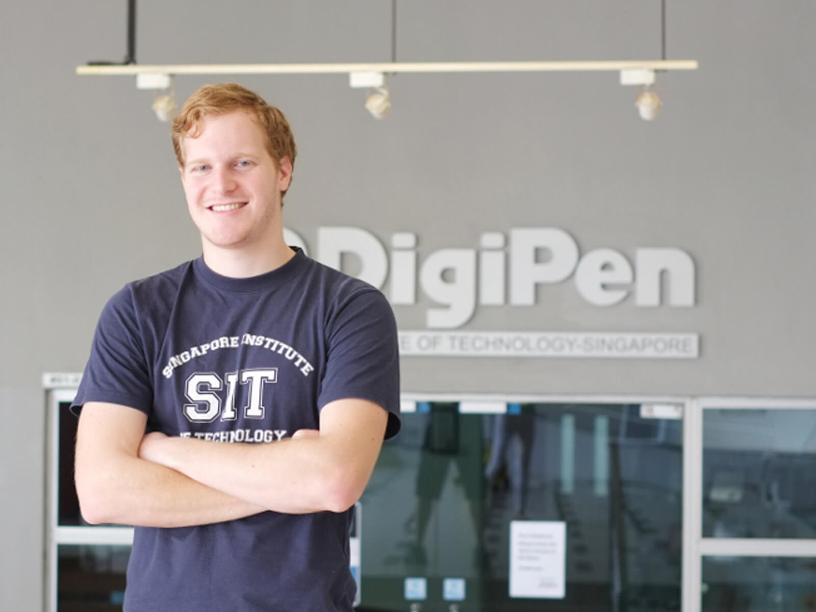 RTIS student Alan Miller poses for a photo arms crossed in front of a building. DigiPen logo is on the building behind him.