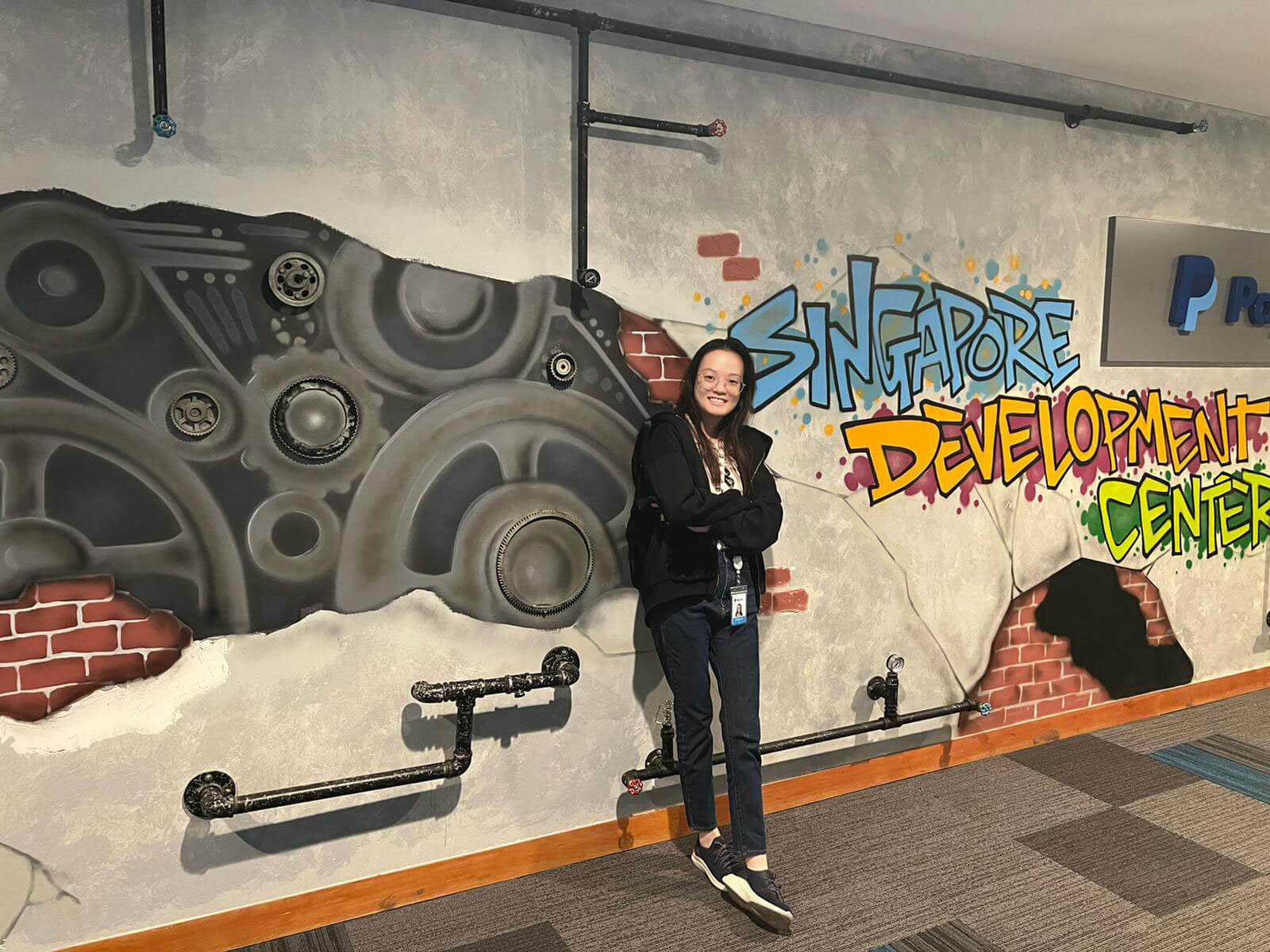 Alumna Jobelle Lim stands against a wall with stylized graffiti that reads 'Singapore Development Center'