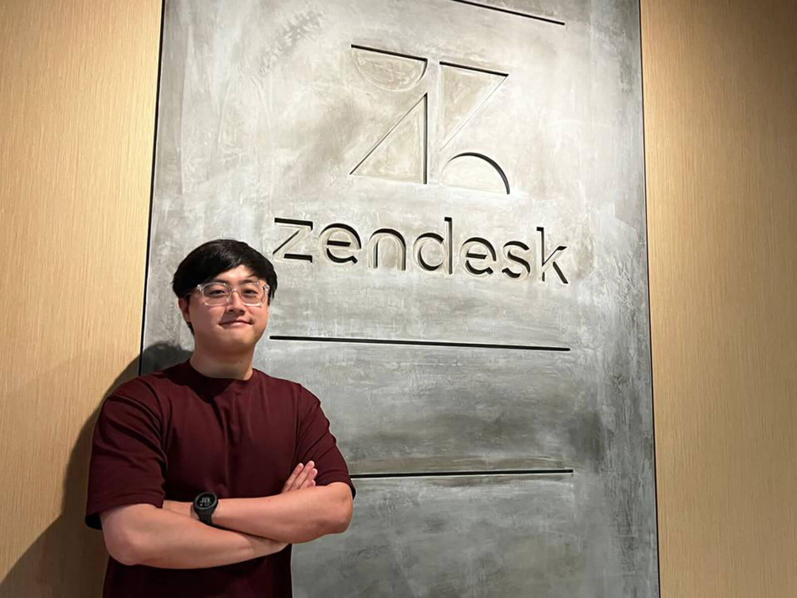 Alumnus Lim Kay Hwee poses in front of a Zendesk logo sign.