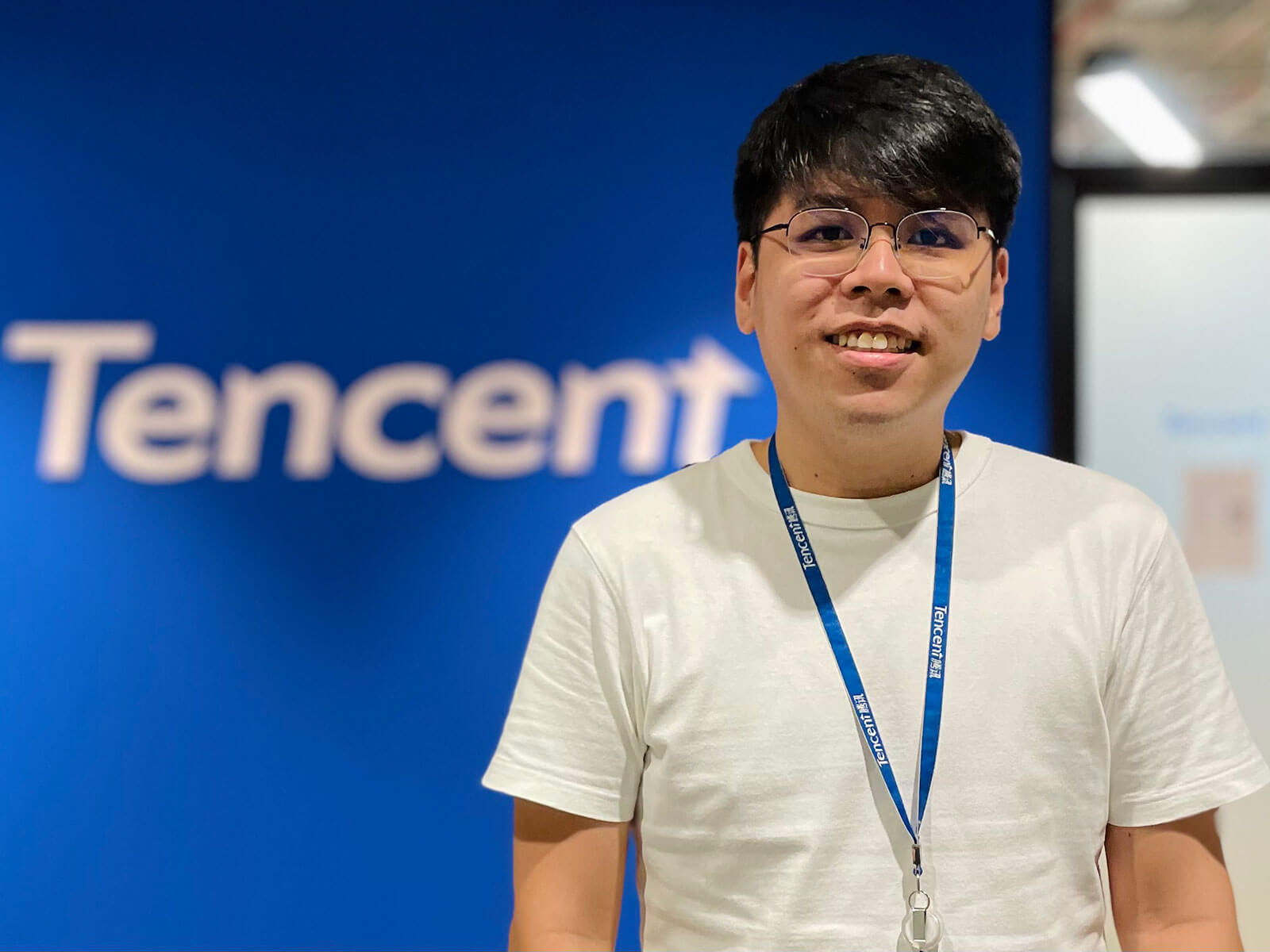 Alumni Mandl Cho stands in front of a blue wall with the Tencent logo on it