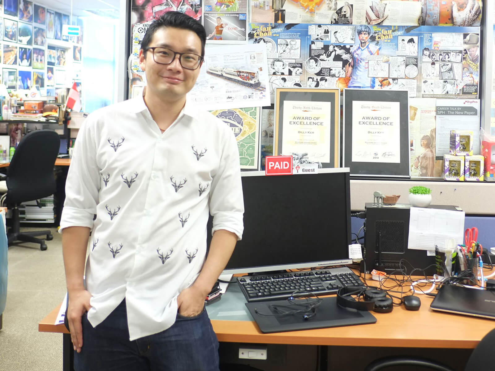 DigiPen graduate Billy Ker stands in an office with walls lined with various colorful printouts of infographics