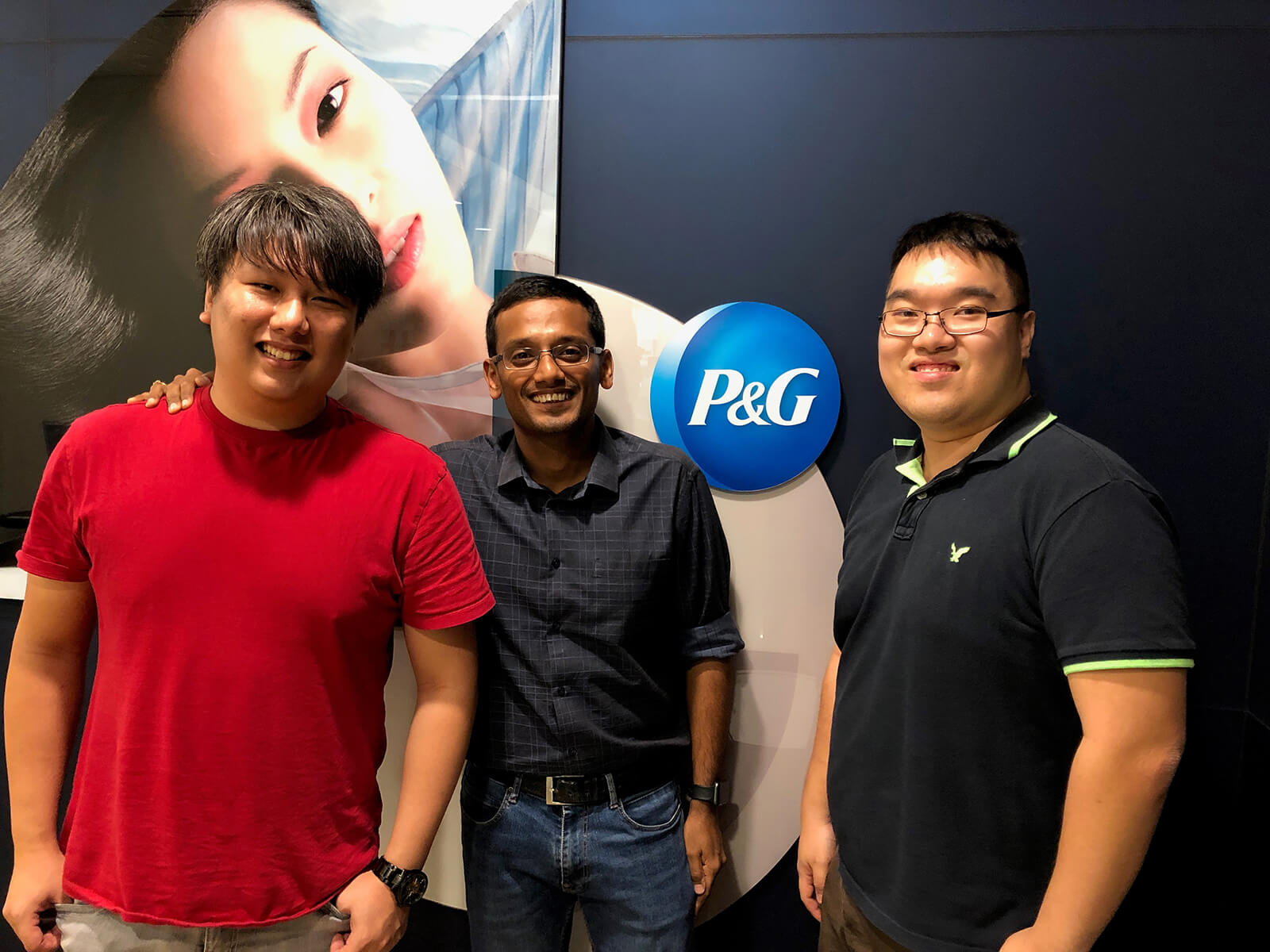 Two SIT-DigiPen (Singapore) graduates stand in front of the Procter &amp; Gamble company logo