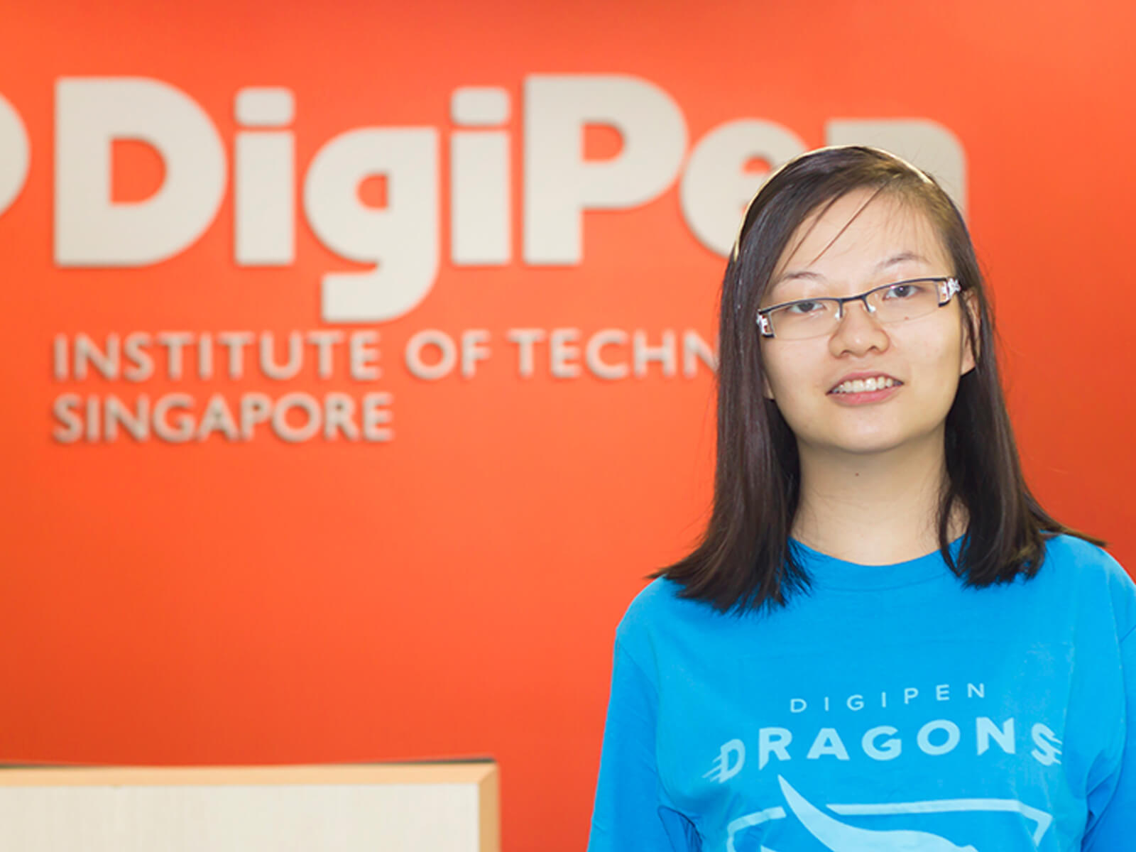 Alumna Chua Fen Ru Jurene posing for a photo in neon blue DigiPen Dragons t-shirt