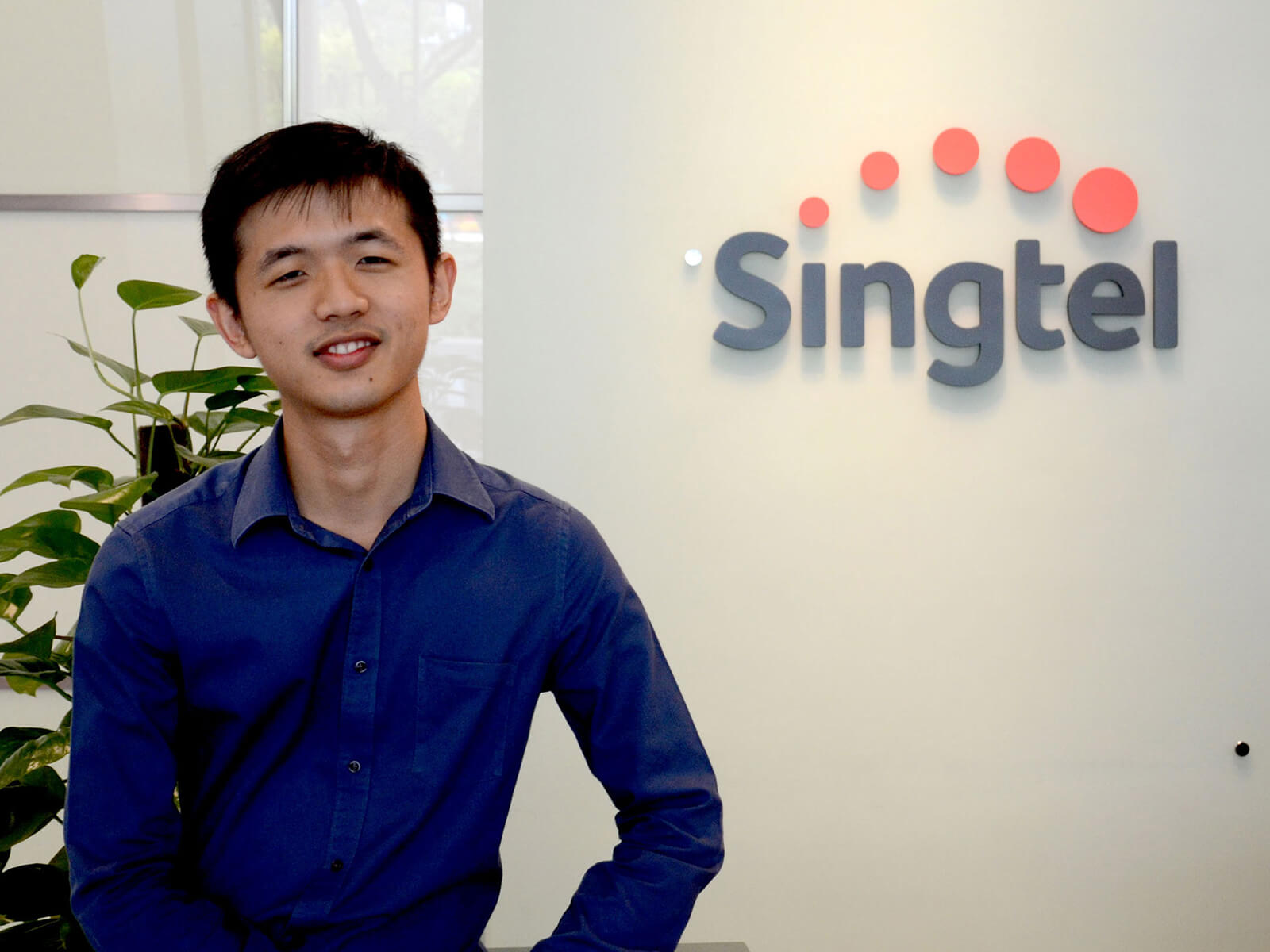 DigiPen (Singapore) BA in Game Design alumnus Daryl Bong poses in front of the Singtel logo