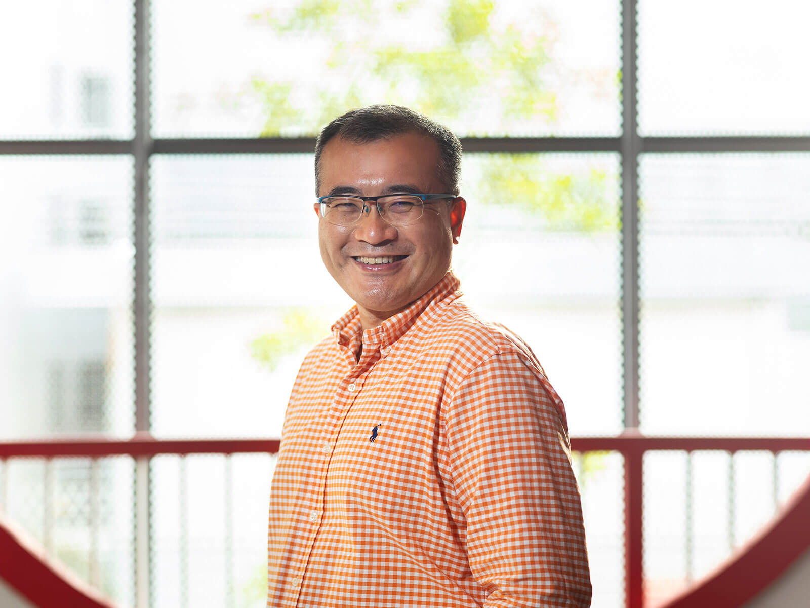 Dr Tang Lang smiles standing in front of a large window