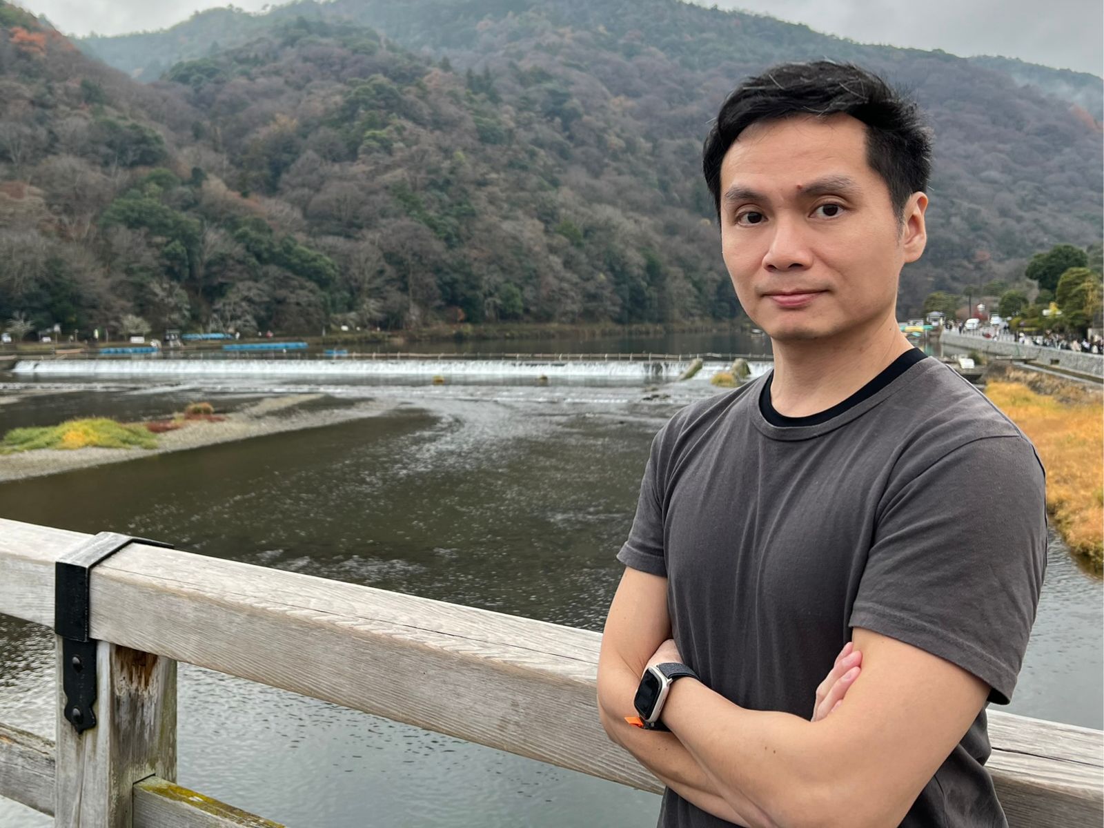 Asian man standing with his arms crossed against a scenic background of a mountain and lake