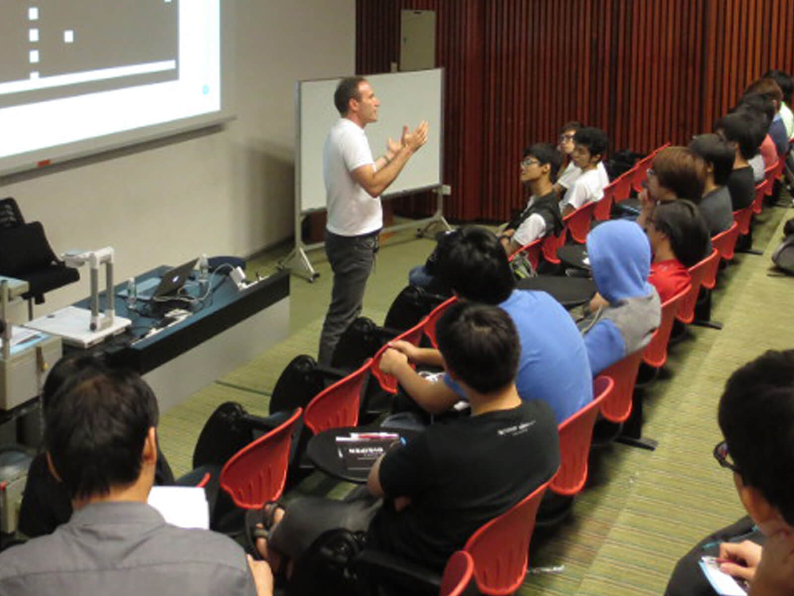 CTO Samir Abou Samra stands speaks to students in a lecture hall with a projection screen behind him