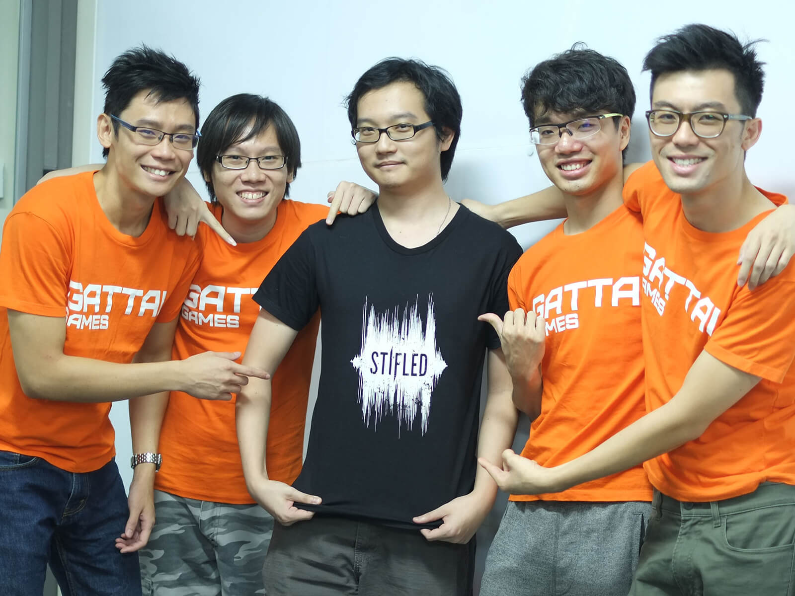 Five members of the Stifled dev team, four in orange t-shirts reading "Gattai Games," and one in a black t-shirt