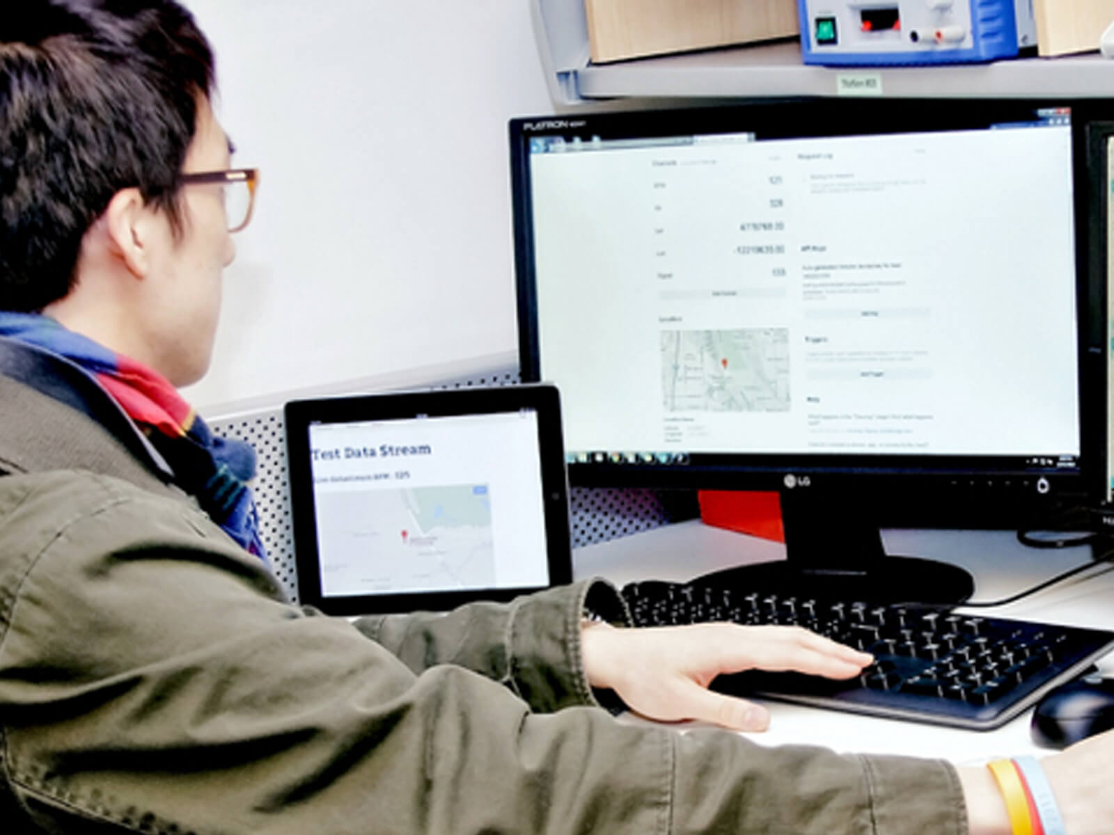 Man sits at a desk looking at two computer monitors. A tablet computer and electrical wiring are also on the desk