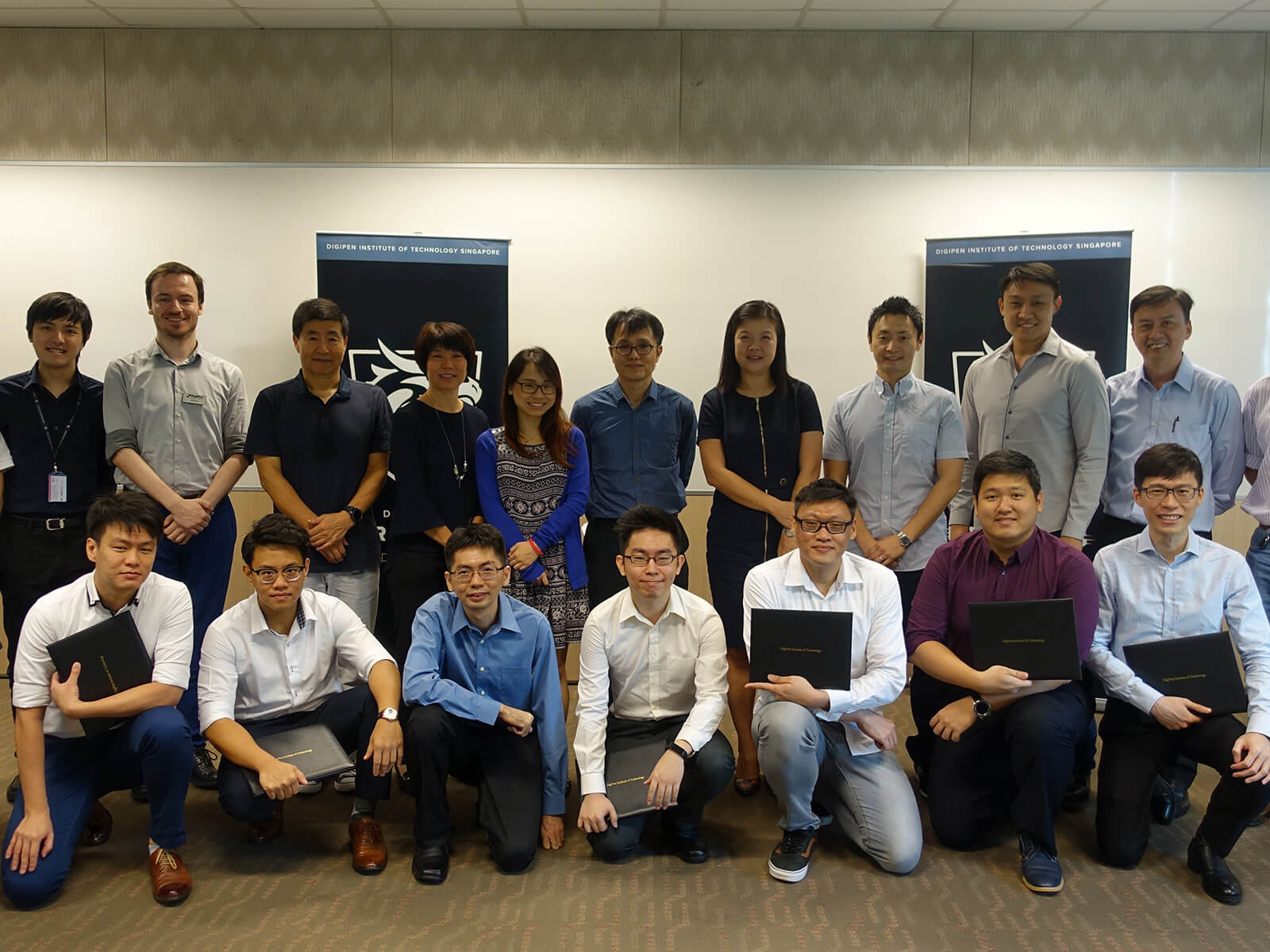 Group photo of 20 people lined up in two rows, including seven CE program graduates in front, holding their diplomas.